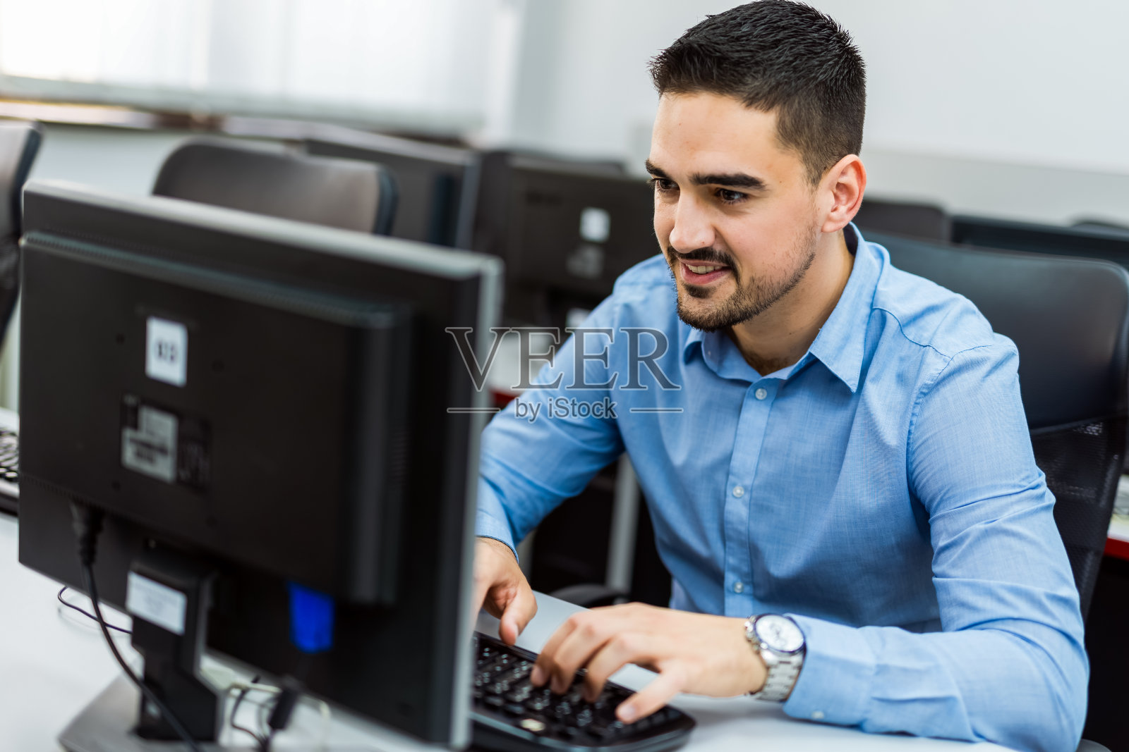 男生在电脑室使用台式电脑。照片摄影图片