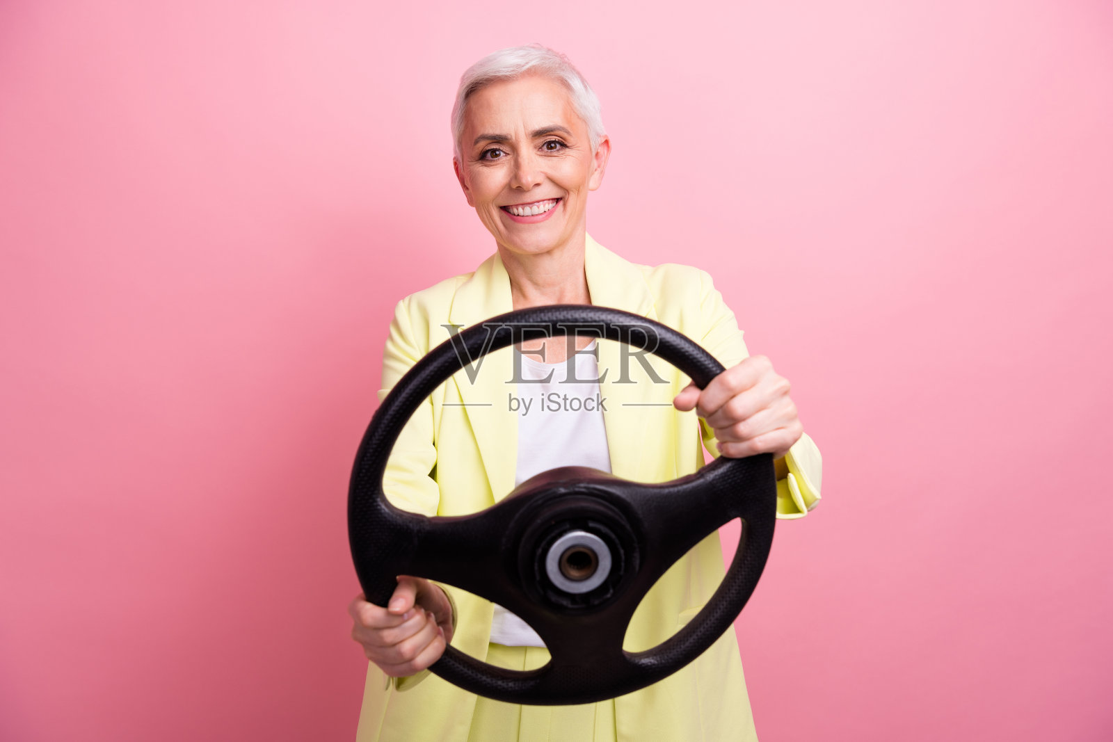 照片中成熟的女商人穿着黄色的正装优雅的驾驶握方向盘慢动作孤立在粉红色的背景照片摄影图片