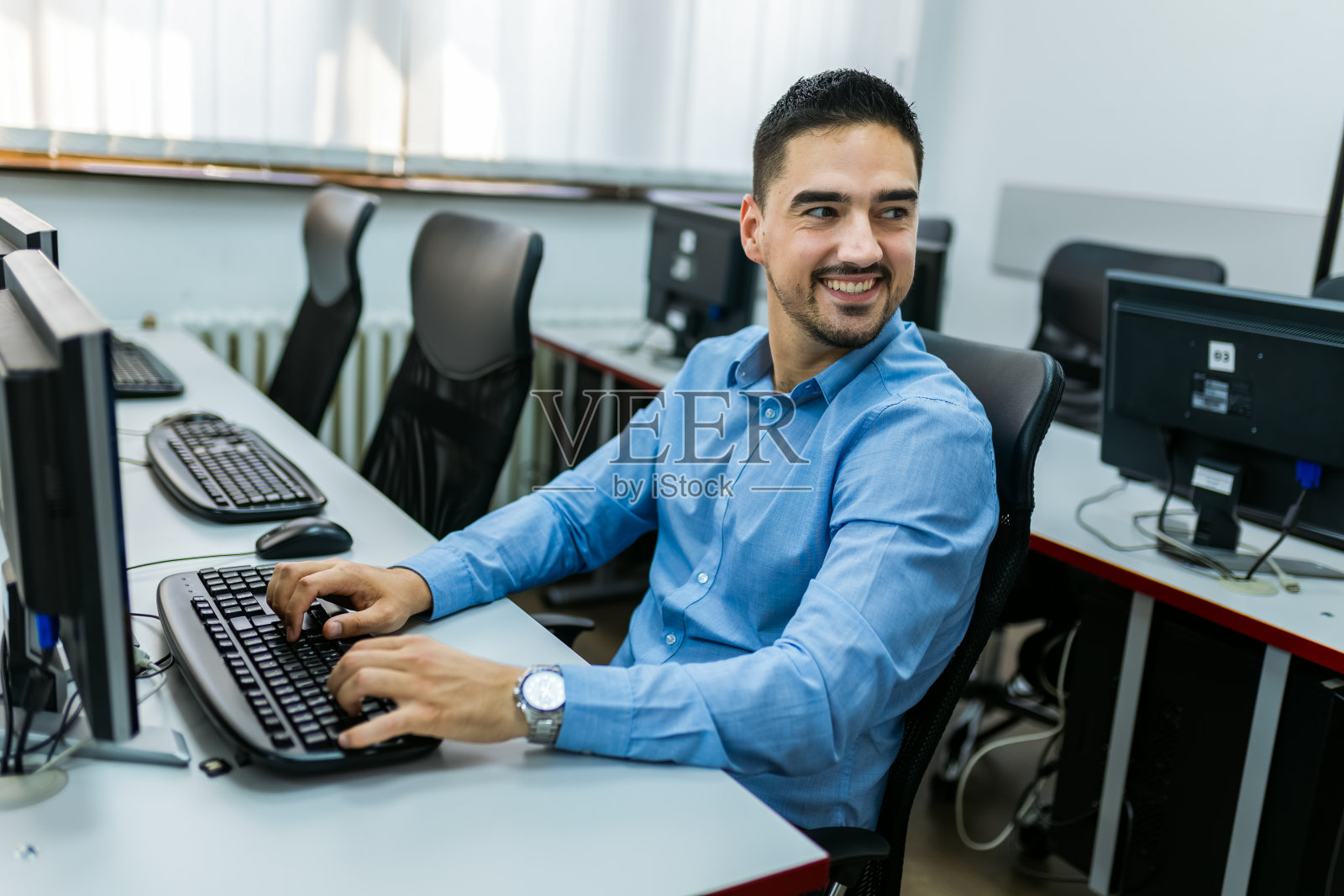 男生在电脑室使用台式电脑。照片摄影图片