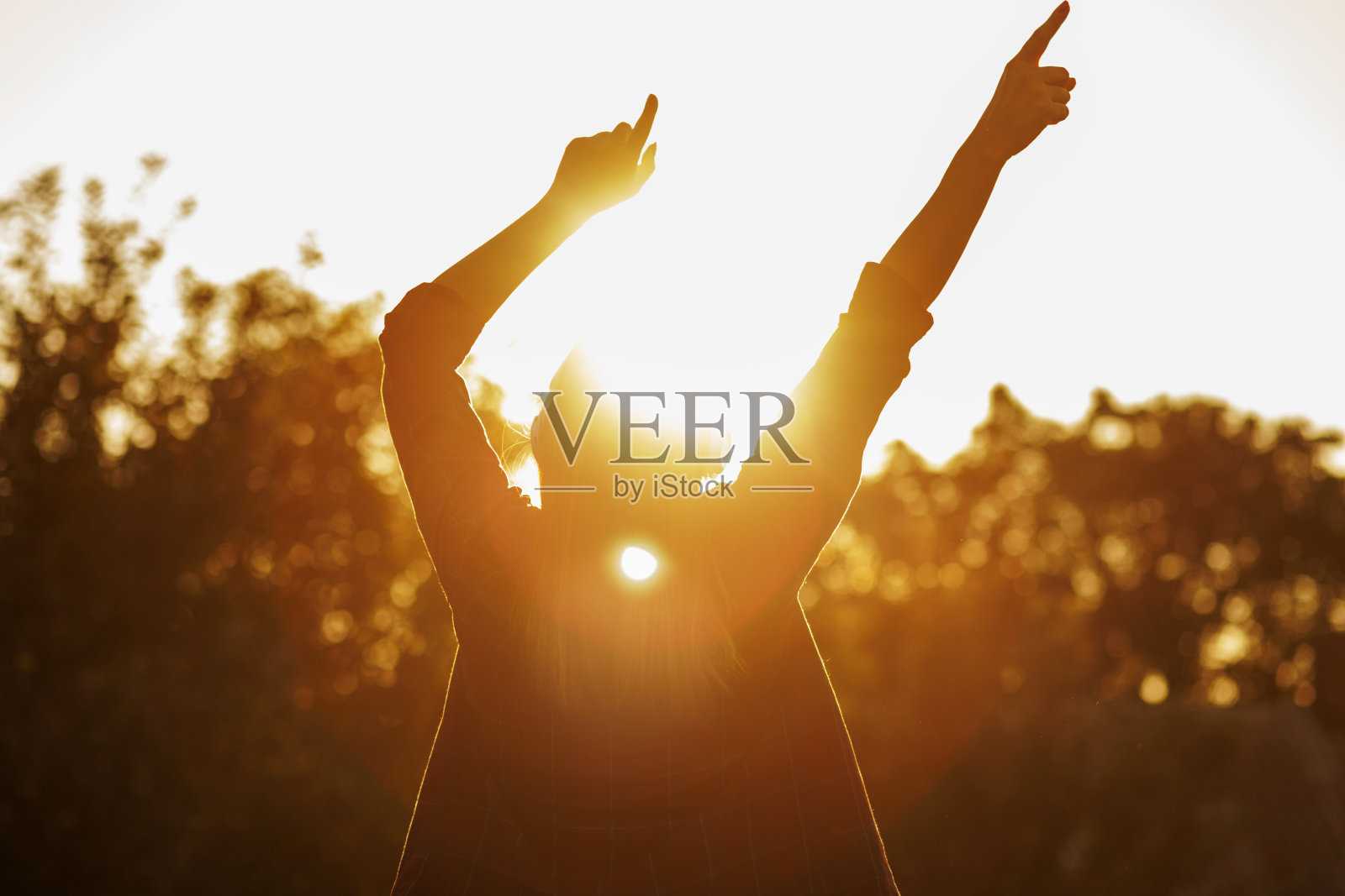 日落时举手的剪影。照片摄影图片