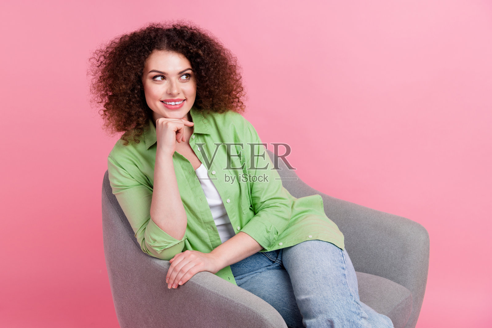 年轻的头脑专家女士的肖像穿着绿色的衬衫，触摸下巴，看起来空的空间，坐在扶手椅孤立在粉红色的背景照片摄影图片