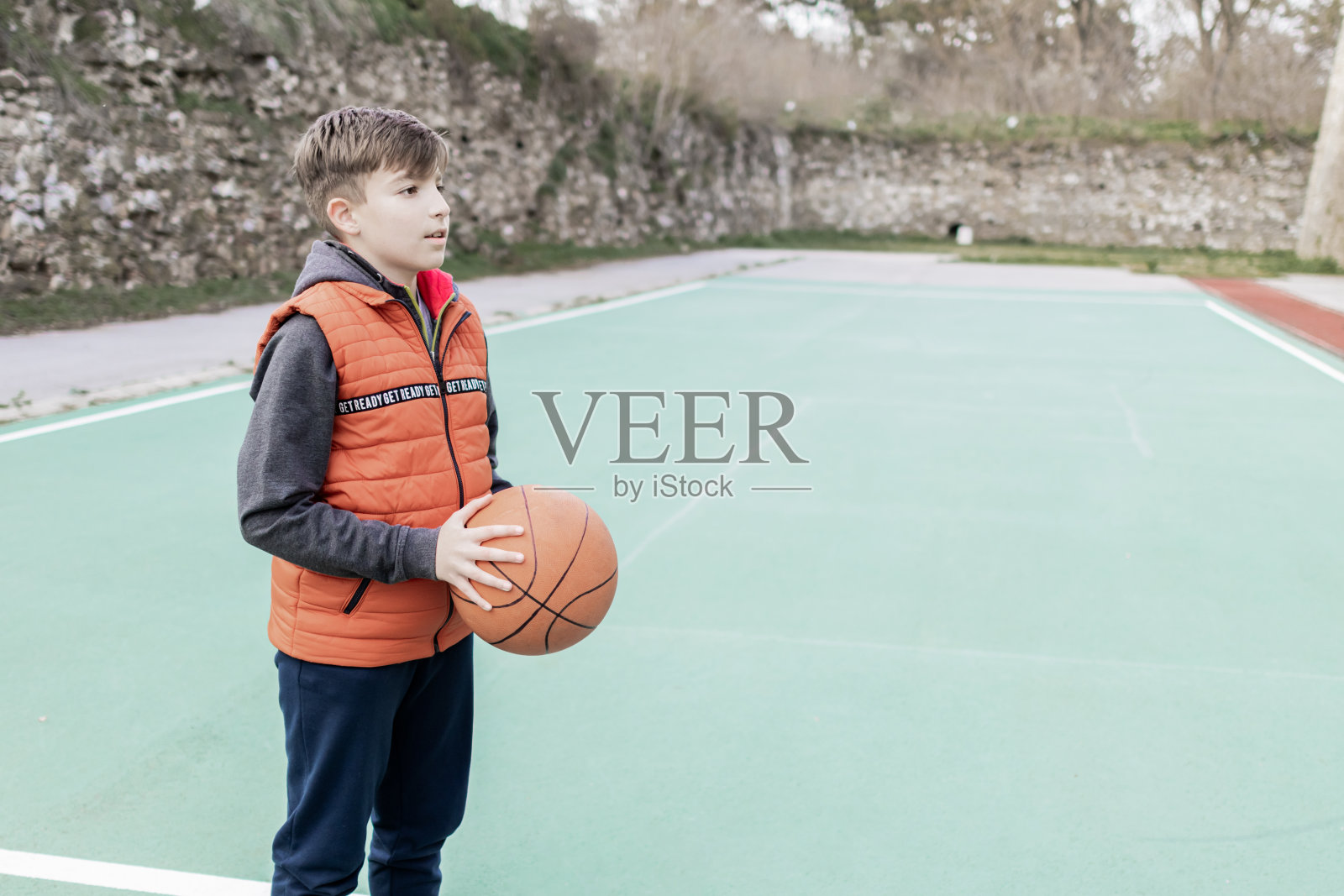 一个男孩在体育场上拿着篮球的照片。照片摄影图片