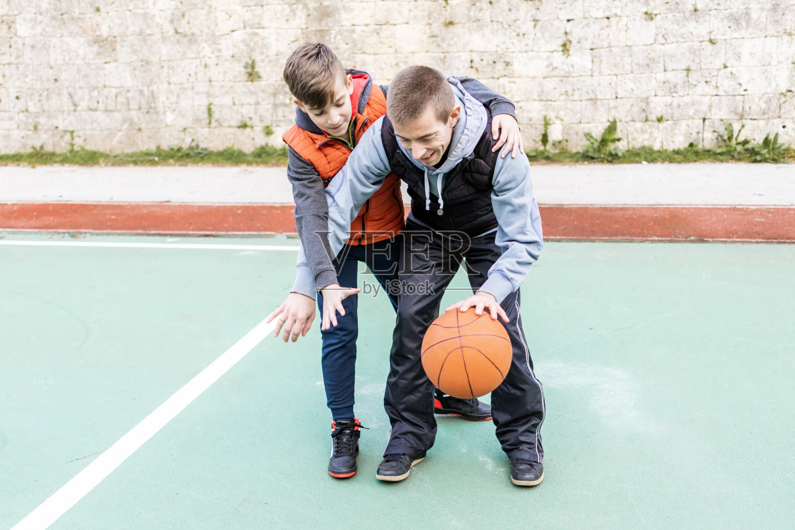 父亲和儿子在球场上打篮球，教小球员。幸福和健康的家庭快乐。户外运动。照片摄影图片