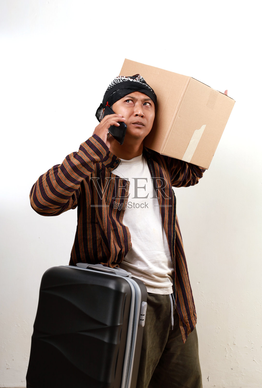 一个穿着爪哇服装的亚洲成年男子拿着行李箱和纸板箱在打电话。返乡概念照片摄影图片