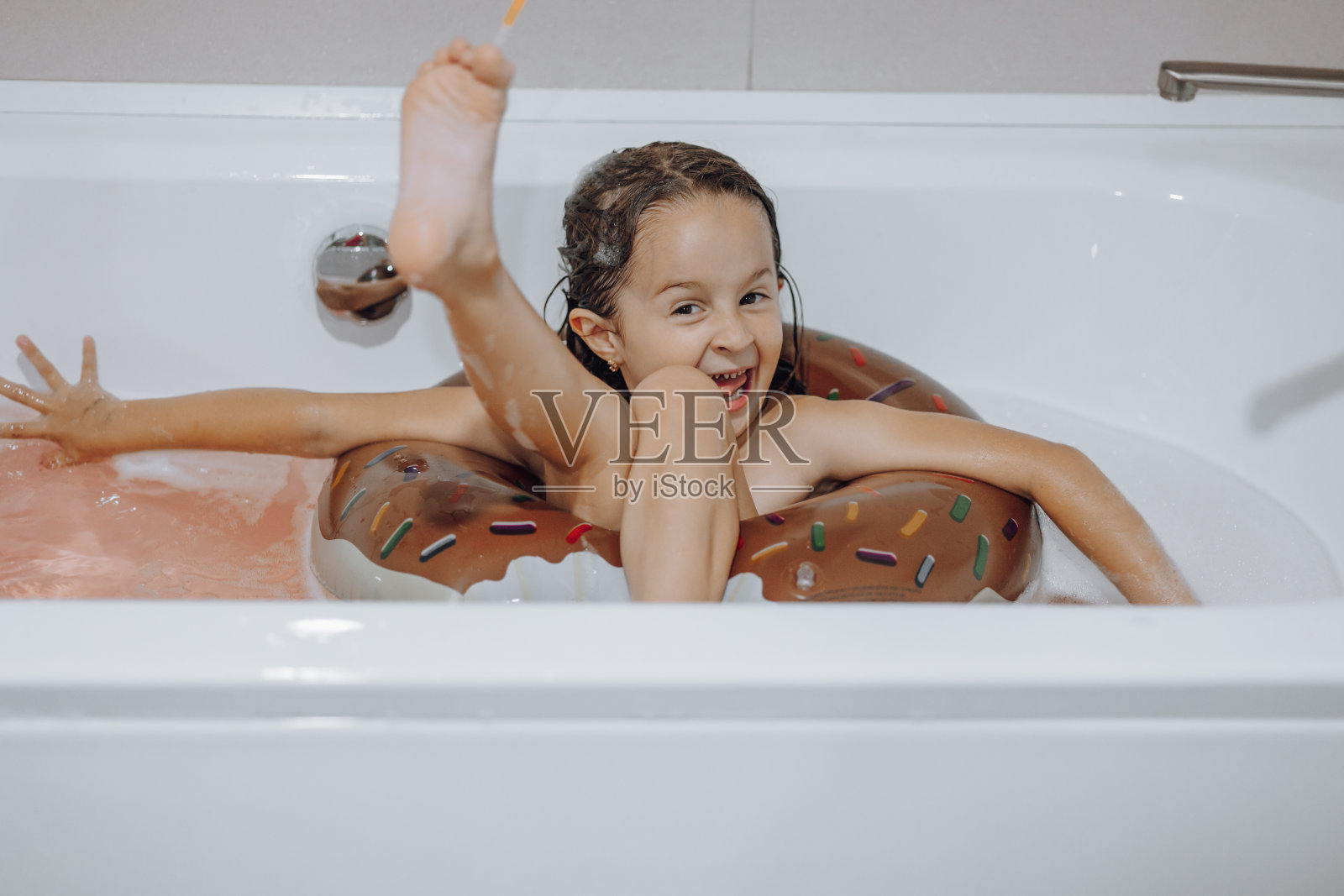 小的，微笑的，漂亮的黑发女孩，长头发，孩子洗澡，洗在一个白色的浴缸与泡沫。有趣的照片。照片摄影图片