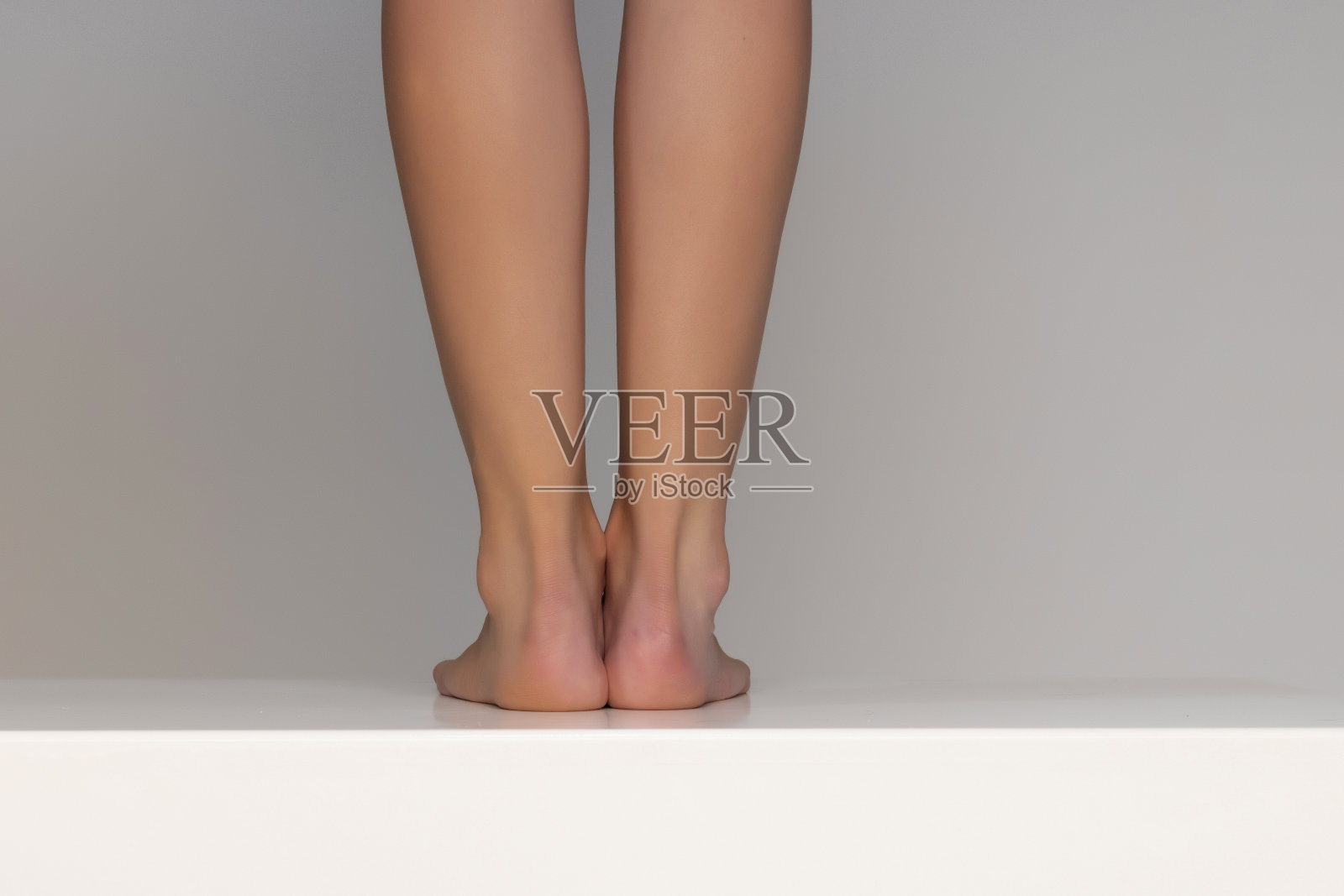 灰色背景上的漂亮女人光着脚和高跟鞋照片摄影图片