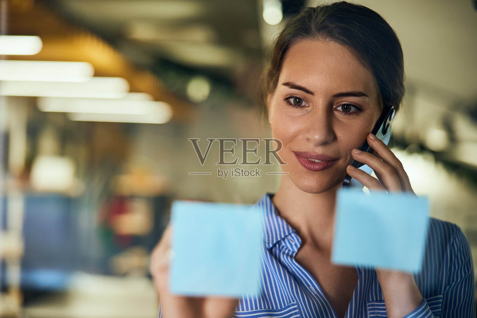 一个美女在玻璃墙上贴便利贴打电话的特写照片。照片摄影图片