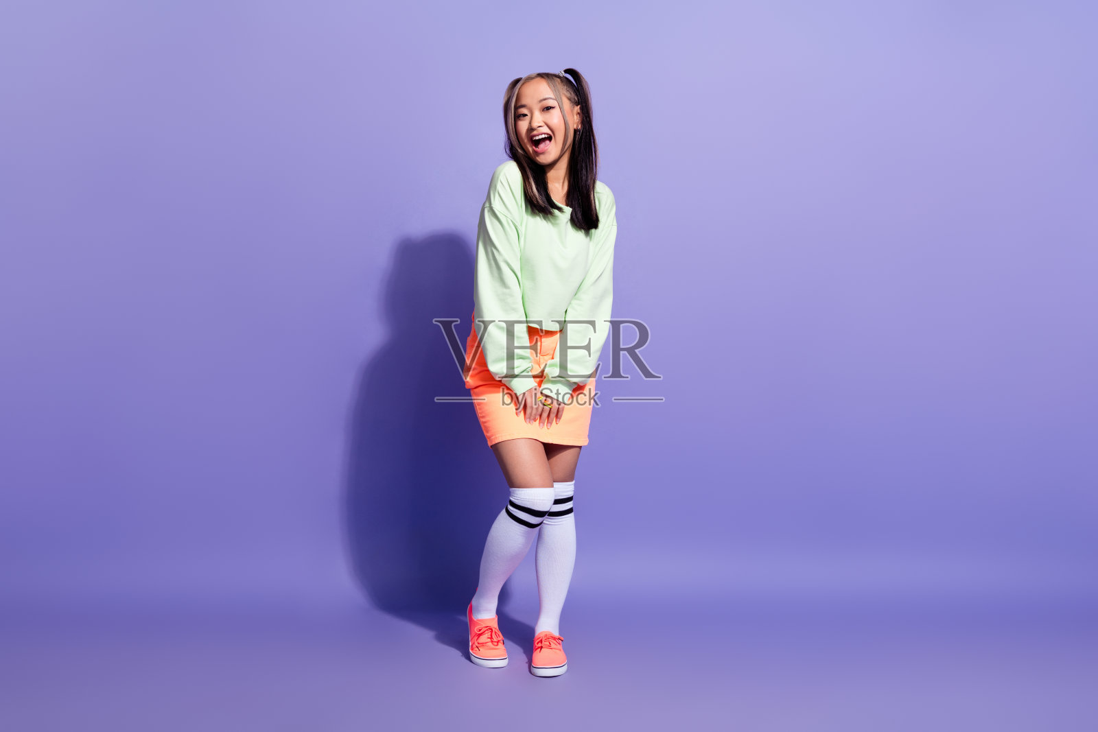 可爱漂亮的日本女人的全身照片，染了色的发型，穿着绿色的运动衫长袜，孤立在紫色的背景上照片摄影图片