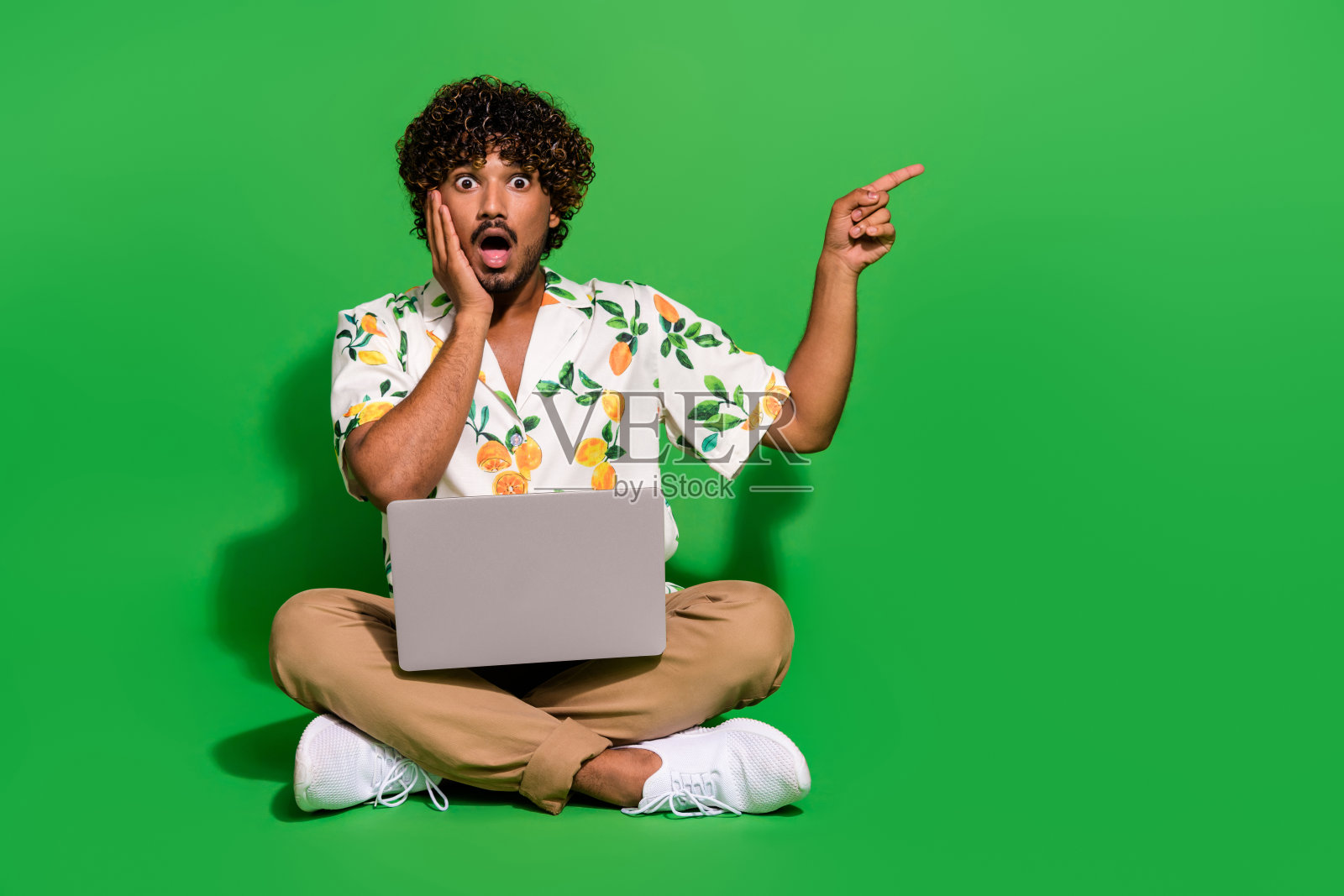 男子全身照片坐在地板上震惊点空旷的空间上网本穿着时尚的柑橘印花衣服孤立的绿色背景照片摄影图片