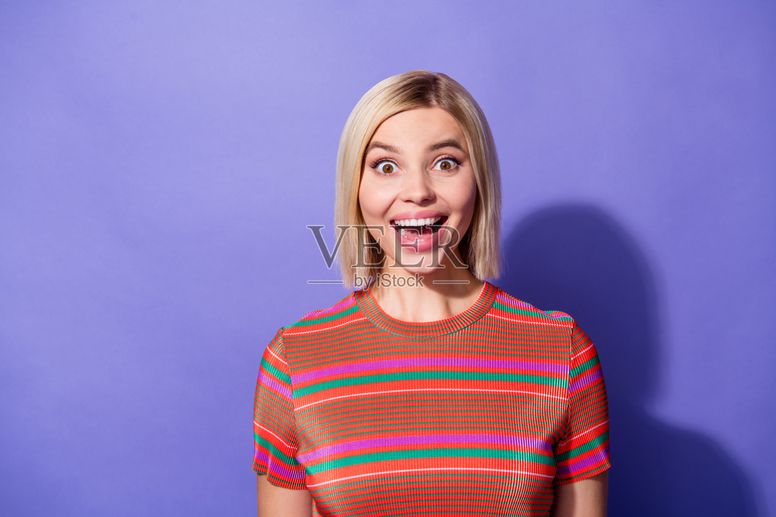 美丽女孩的肖像穿着橙色条纹t恤震惊惊人的消息，她怀孕印象深刻的反应孤立在紫色的背景照片摄影图片