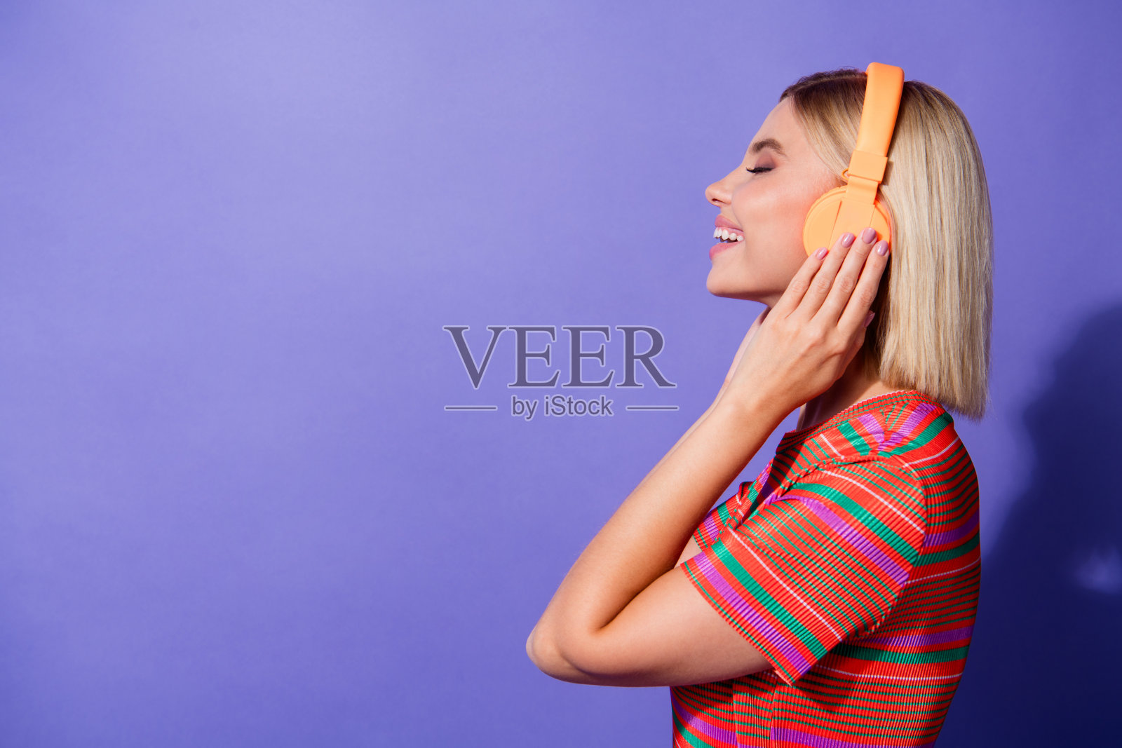 美洛曼年轻的女孩一边享受无线橙色耳机音乐的最佳排行榜播放列表孤立的紫色背景照片照片摄影图片