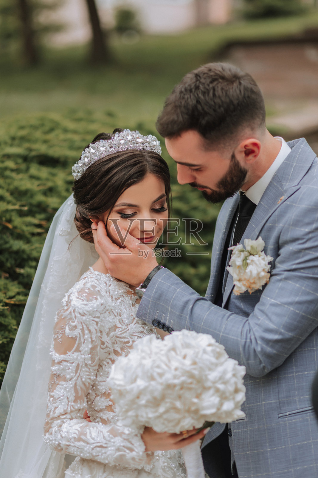 在公园里举行欧洲婚礼的夫妇。新娘穿着一件有袖子的漂亮礼服，头上戴着一顶王冠。新郎留着白胡子，穿着经典西装照片摄影图片