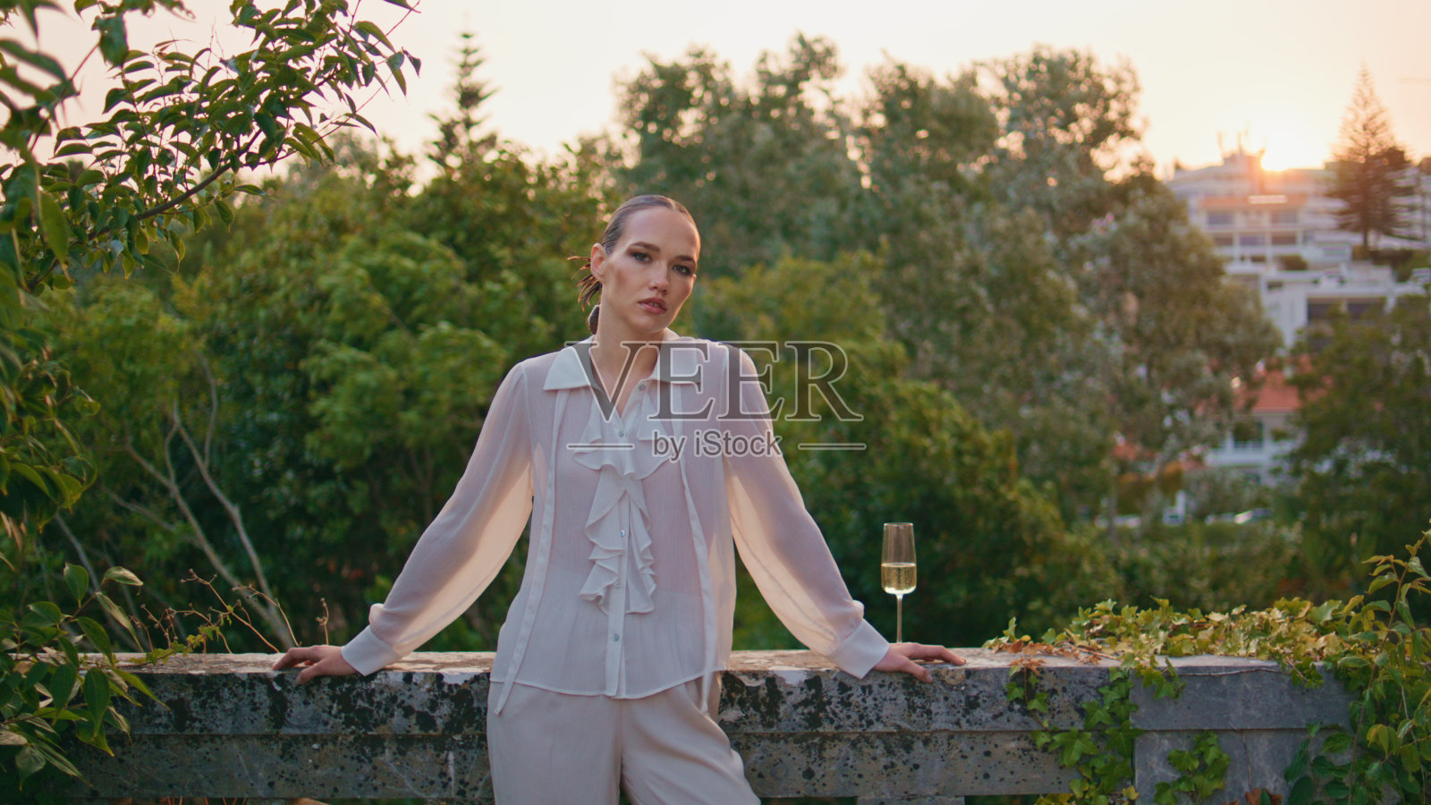 自信的女人在老建筑的阳台上拍照。拿着酒杯的漂亮女孩。照片摄影图片