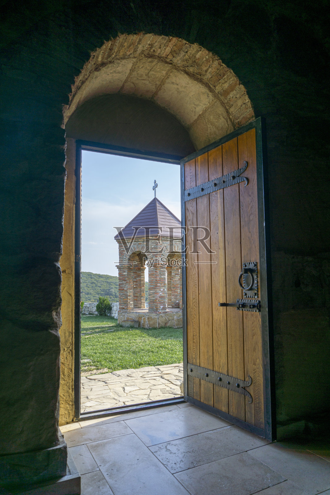 从圣乔治教堂透过敞开的门看到钟楼。砖砌的拱门和屋顶上的十字架。木门，有把手和铁门栓。照片摄影图片
