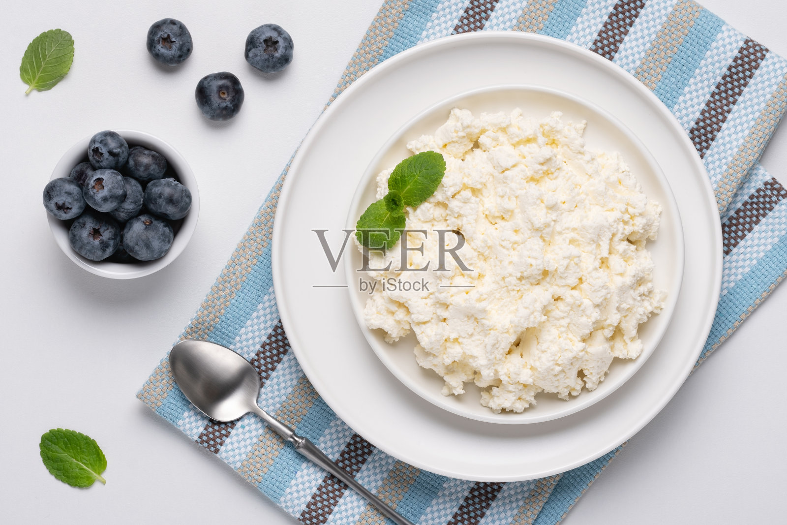 白桌子上的白干酪配蓝莓和薄荷。碗里的白干酪。前视图。乳制品照片摄影图片