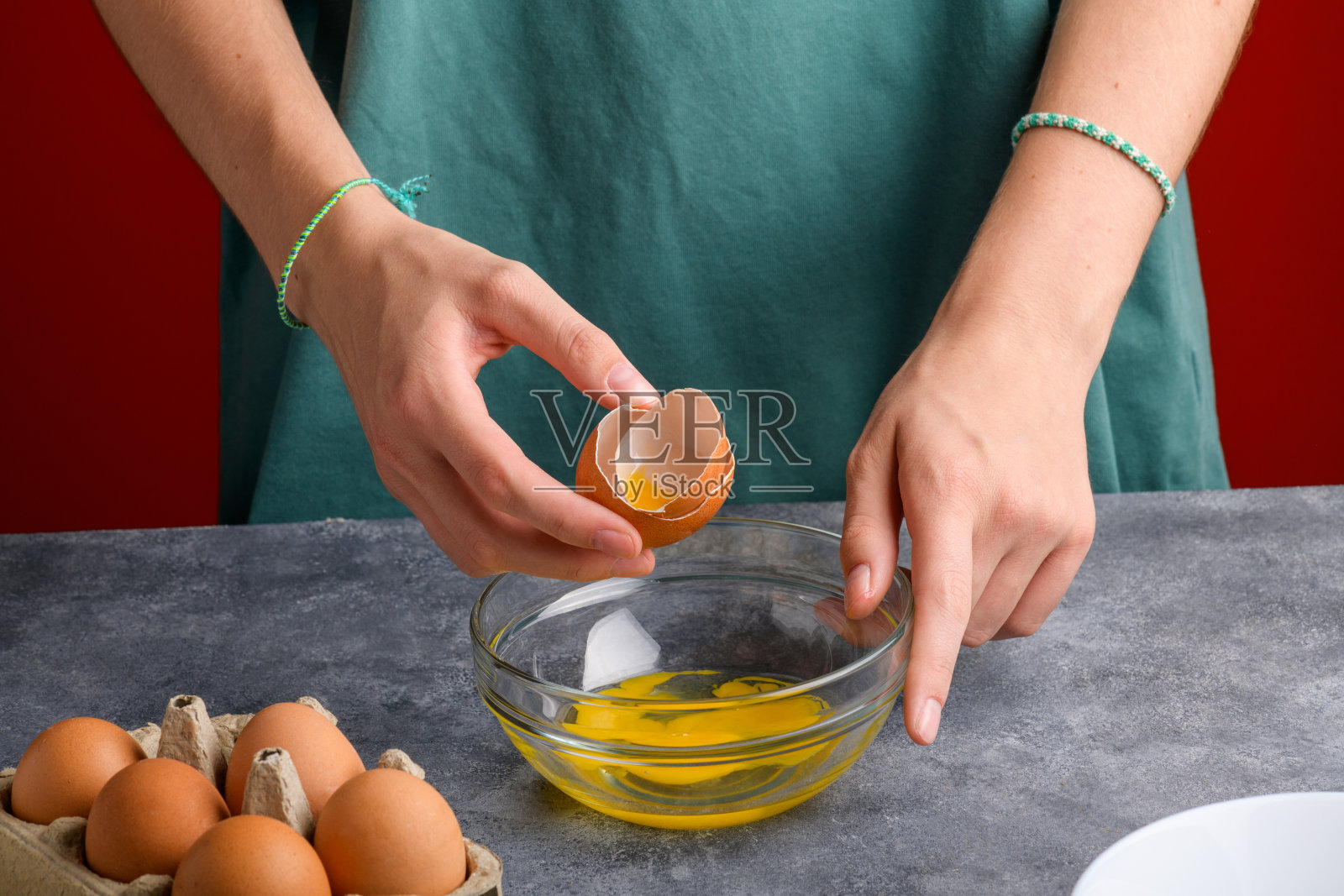 灰色的厨房桌子上，一个女人的手把打碎的鸡蛋壳放进一个透明的玻璃碗里照片摄影图片