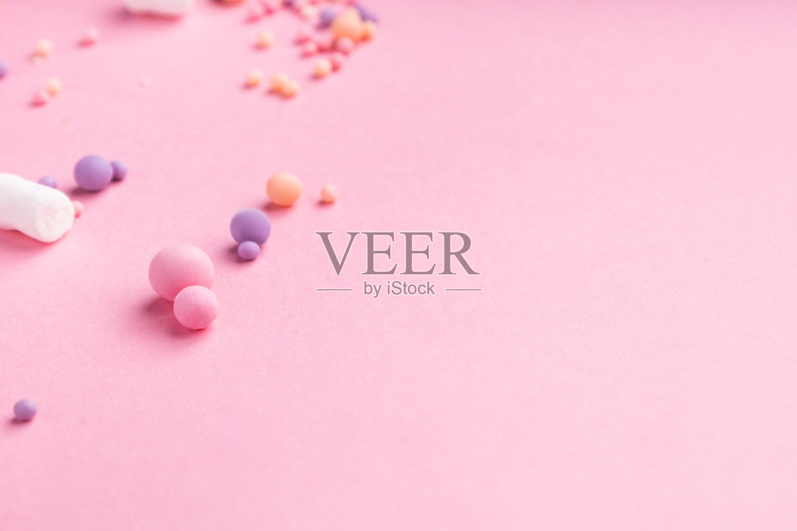 粉红色的背景上点缀着不同颜色和大小的小糖果和棉花糖。大量的空白空间照片摄影图片