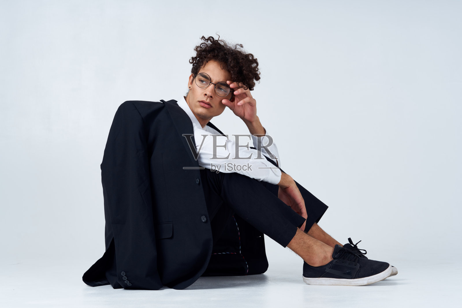 一个时髦的卷发男人，穿着经典的西装和运动鞋，坐在室内摄影工作室的地板上照片摄影图片