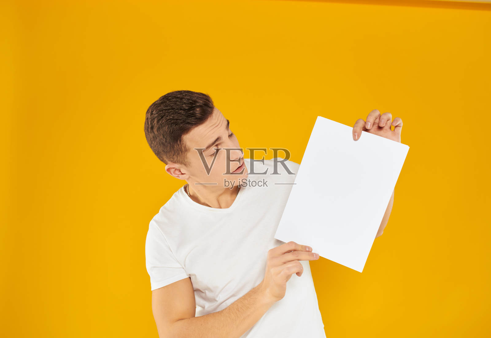 小伙子用一张白色的纸在黄色的背景上空白的名片做广告照片摄影图片