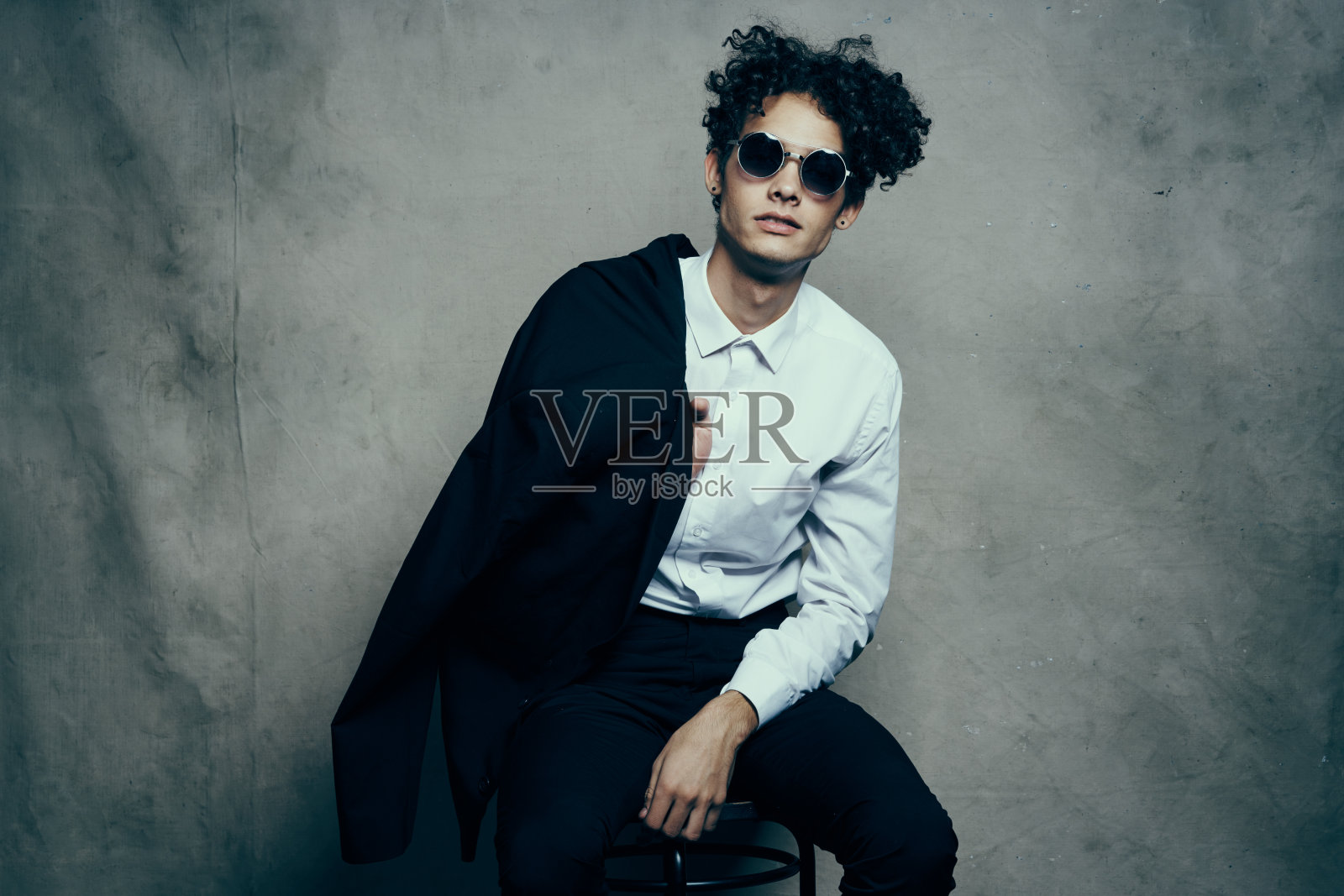 一个时髦的家伙，在室内的织物背景上有一头卷发，肩上披着一件夹克照片摄影图片