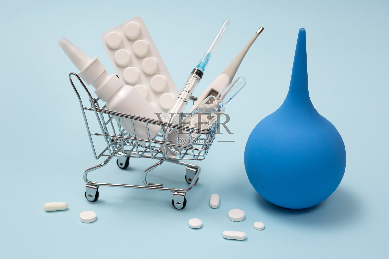 蓝色背景的购物篮里装着药片、鼻喷雾剂、注射器、温度计和灌肠剂照片摄影图片