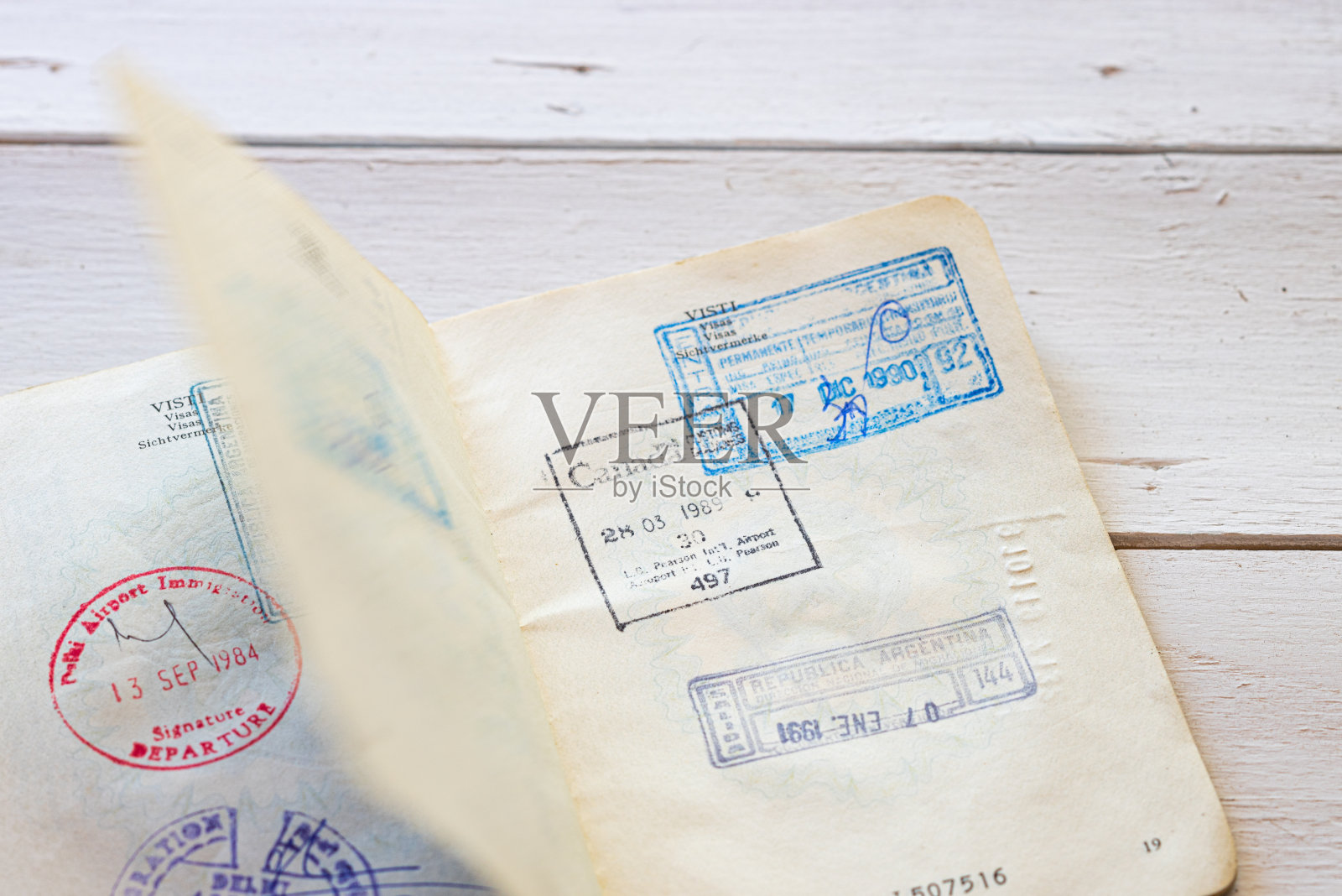 护照上的旧移民印章。移民签证的旧意大利护照在一个白色的木制背景。照片摄影图片