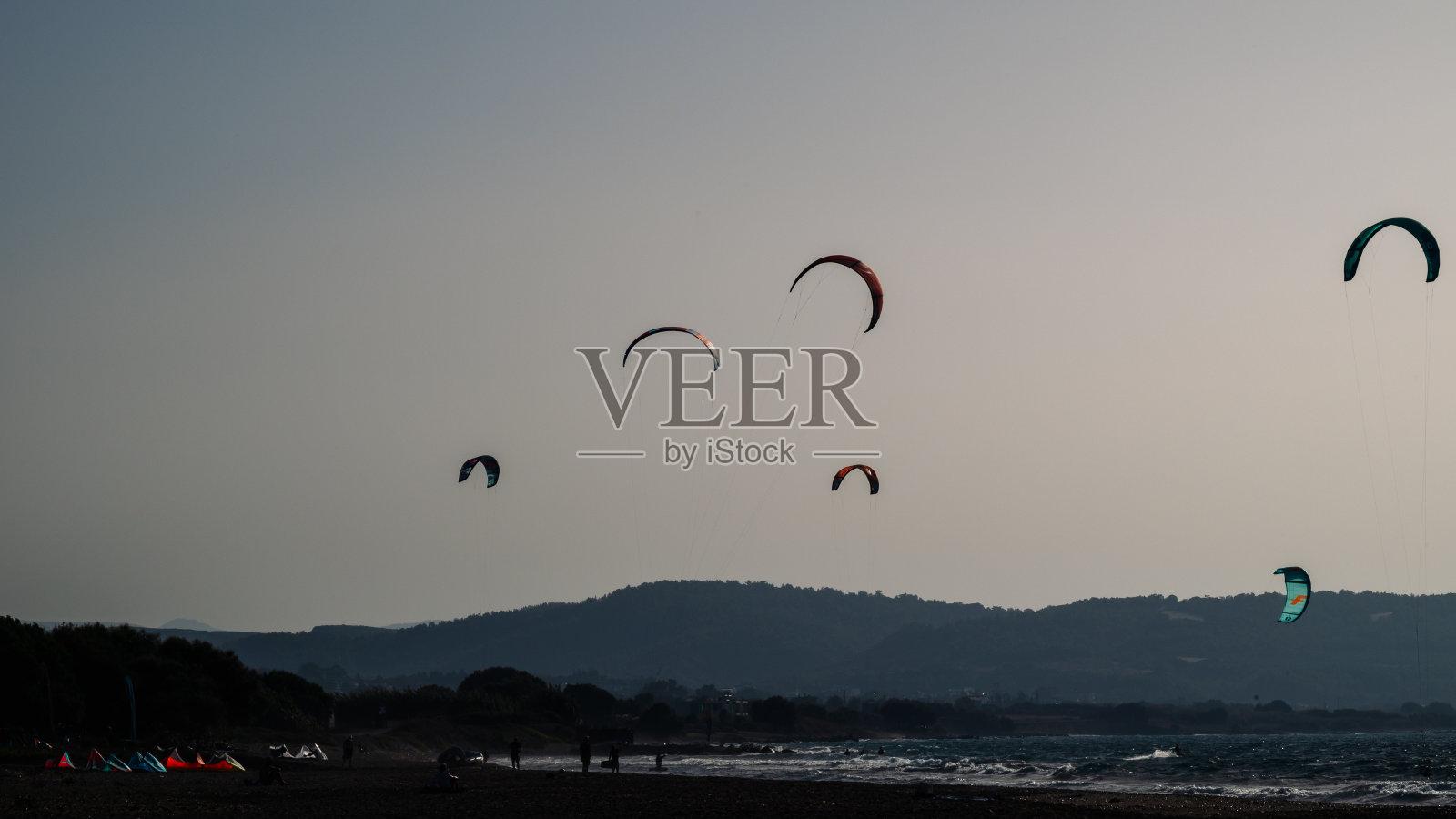 年轻人在日落时在海里滑风帆。降落伞的剪影。照片摄影图片