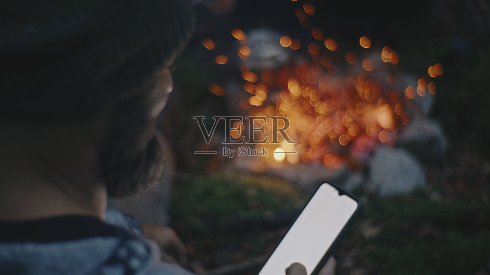 假期在森林露营时，一名男子在营火旁使用智能手机照片摄影图片