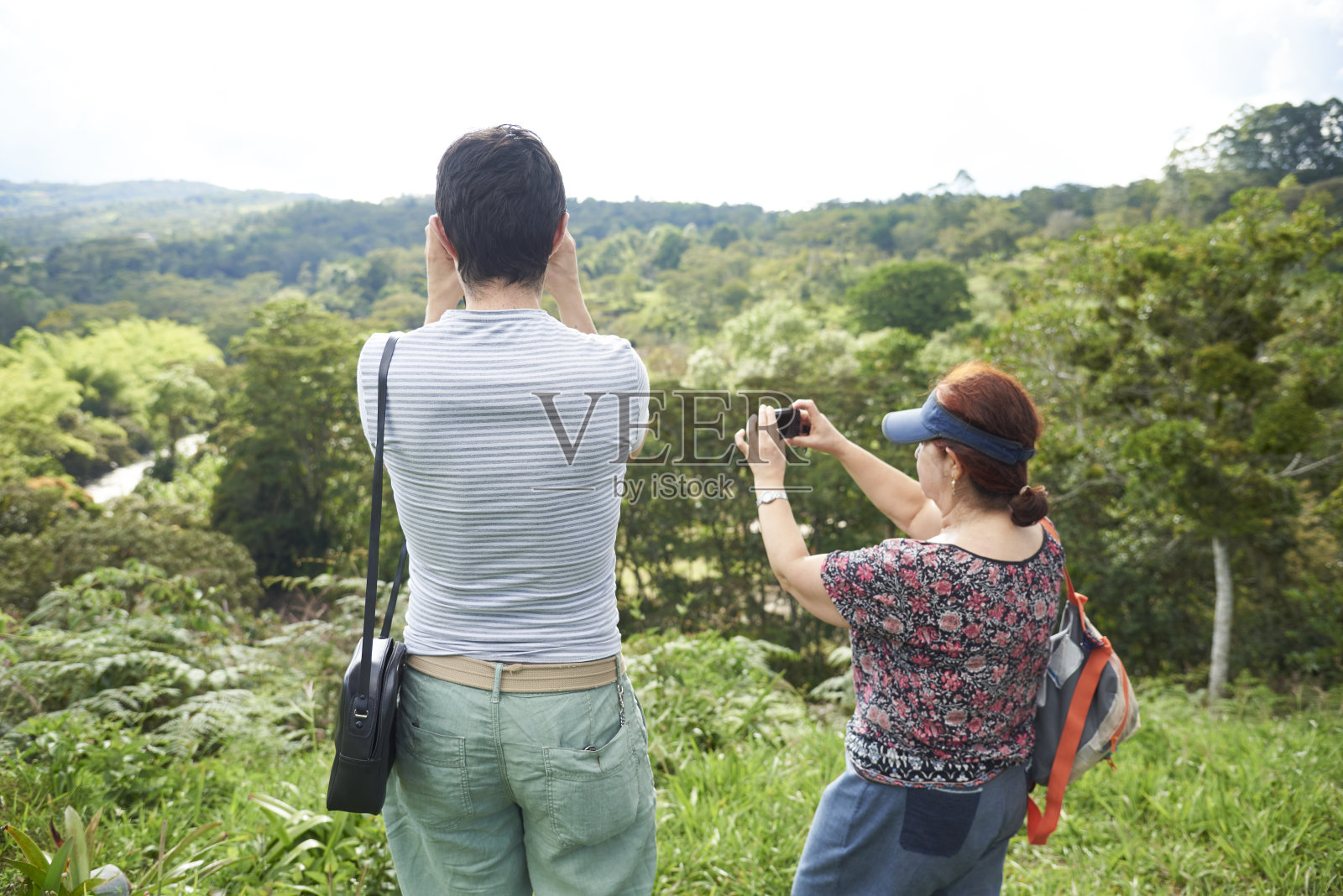 母亲带着已成年的儿子享受旅行，儿子拿着望远镜看风景，母亲则在一旁拍照。照片摄影图片