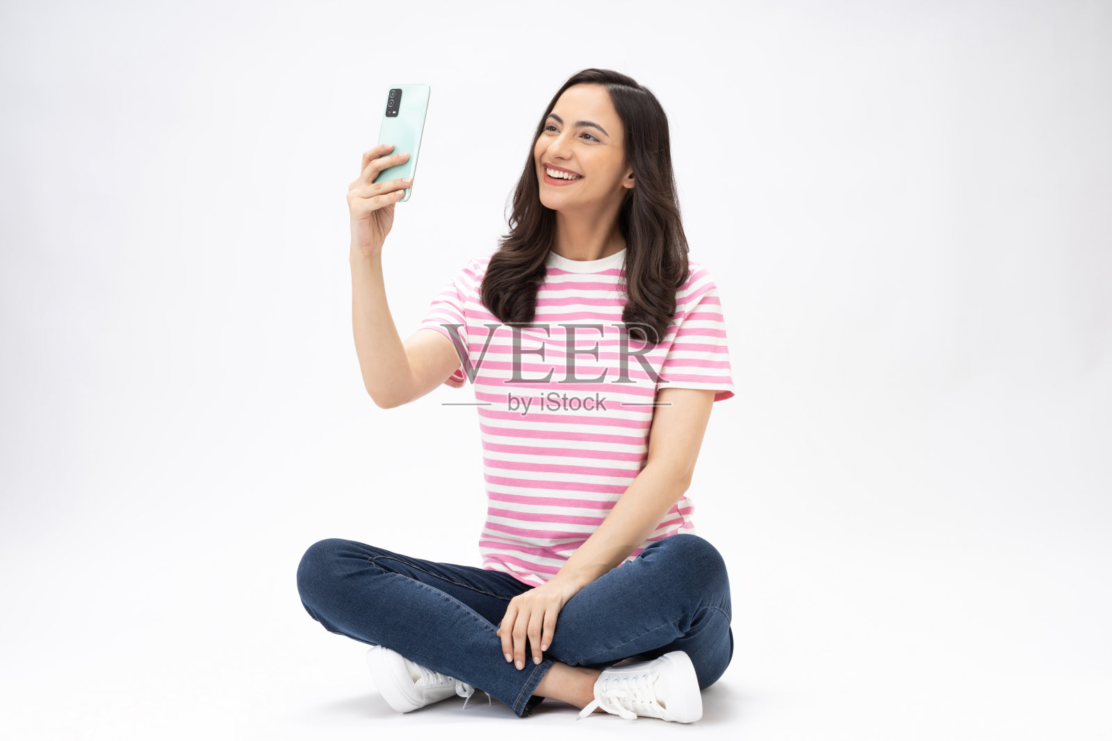 漂亮的年轻女孩坐在地板上自拍，穿着时髦的衣服，孤立在白色背景的照片照片摄影图片