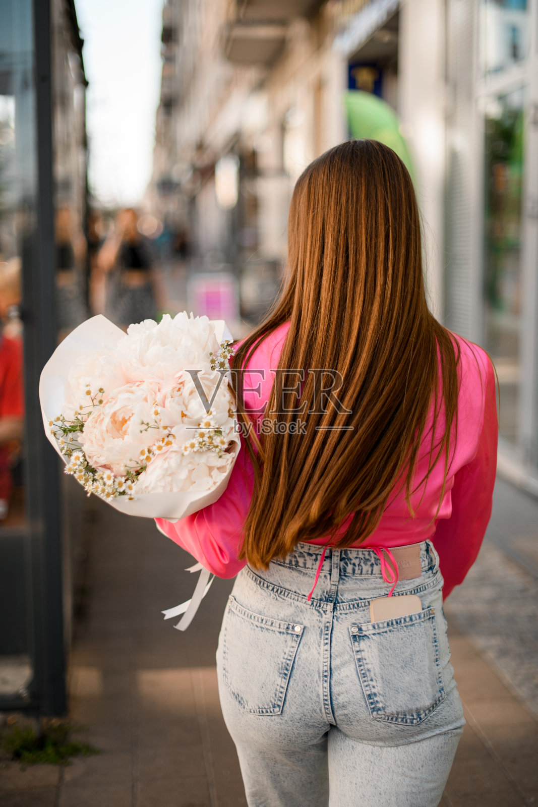 穿着牛仔裤和粉色衬衫的年轻女子拿着一束牡丹从镜头前走了出来照片摄影图片