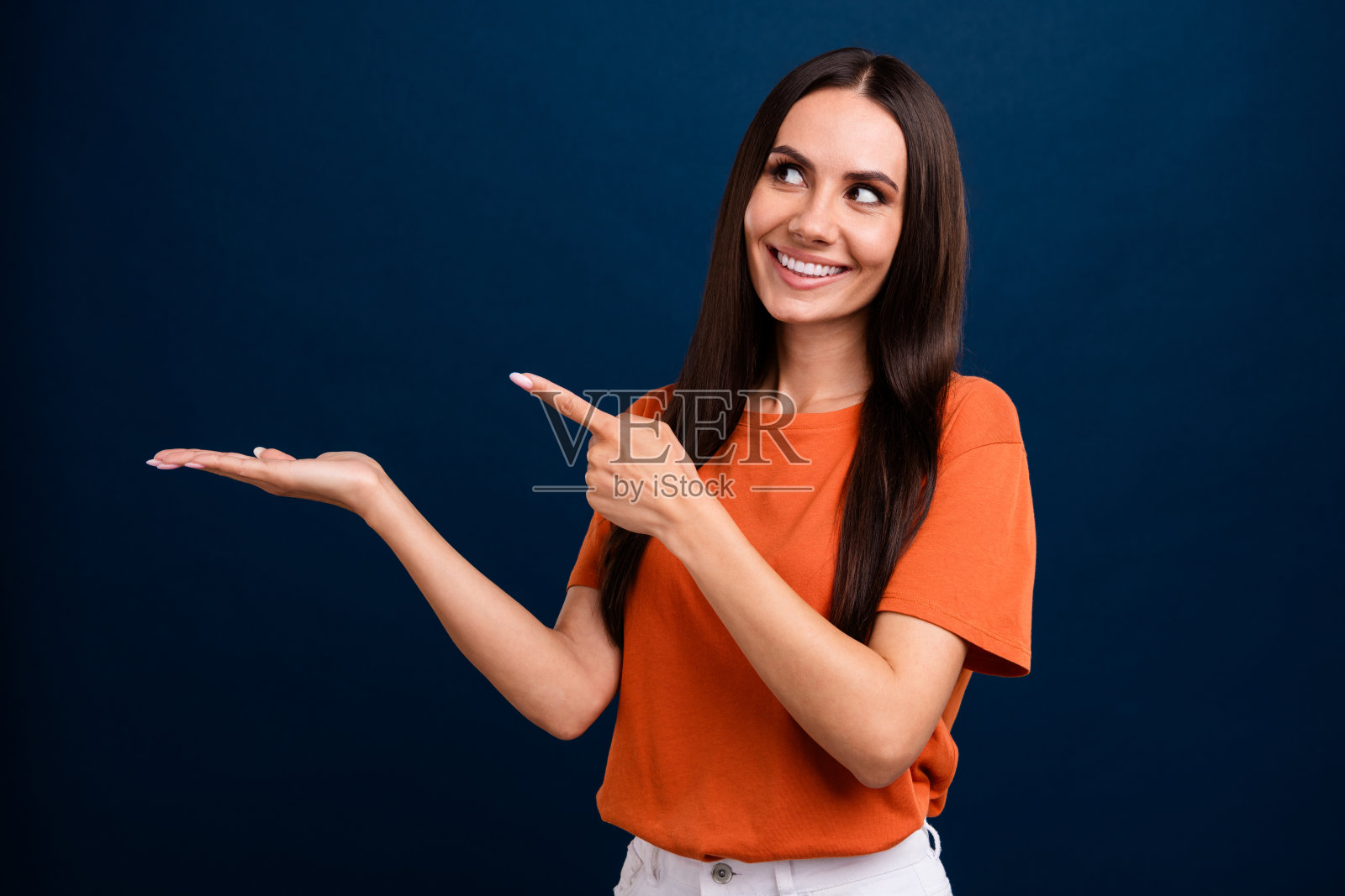 心情好的女人穿着橙色t恤的照片展示了在深蓝色的背景上引导空白的空间照片摄影图片