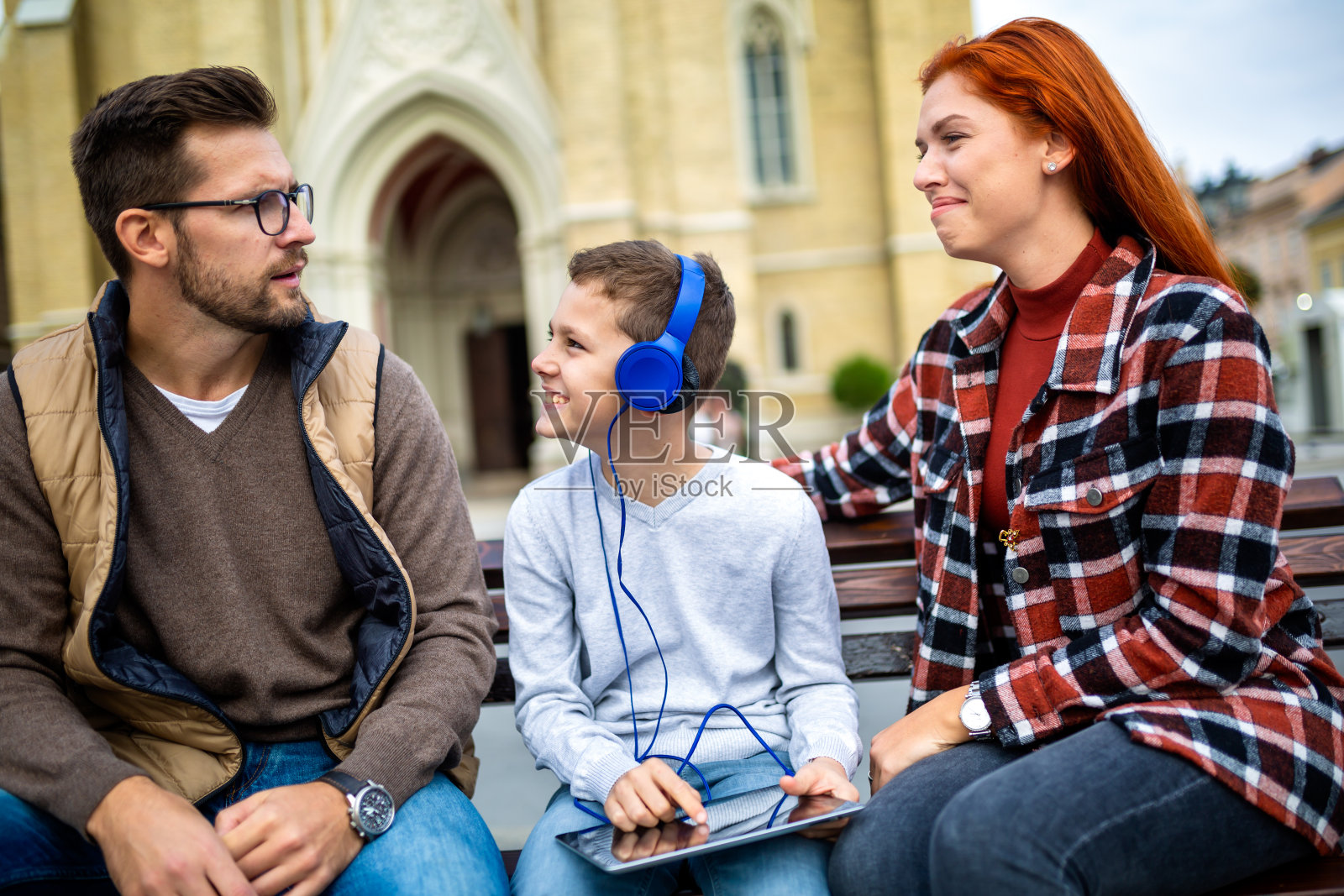 一家人坐在长凳上，放松地使用电子设备，浏览互联网。照片摄影图片