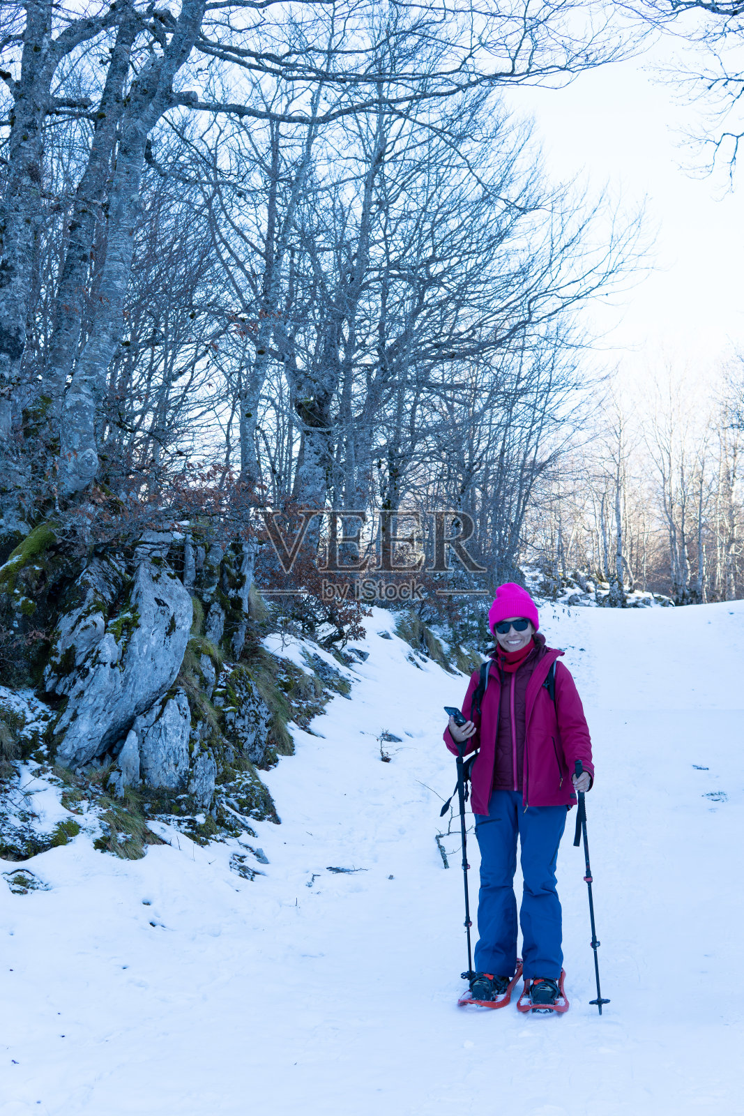 一个女人穿着雪鞋在雪地里拿着手机。微笑着看着镜头。照片摄影图片
