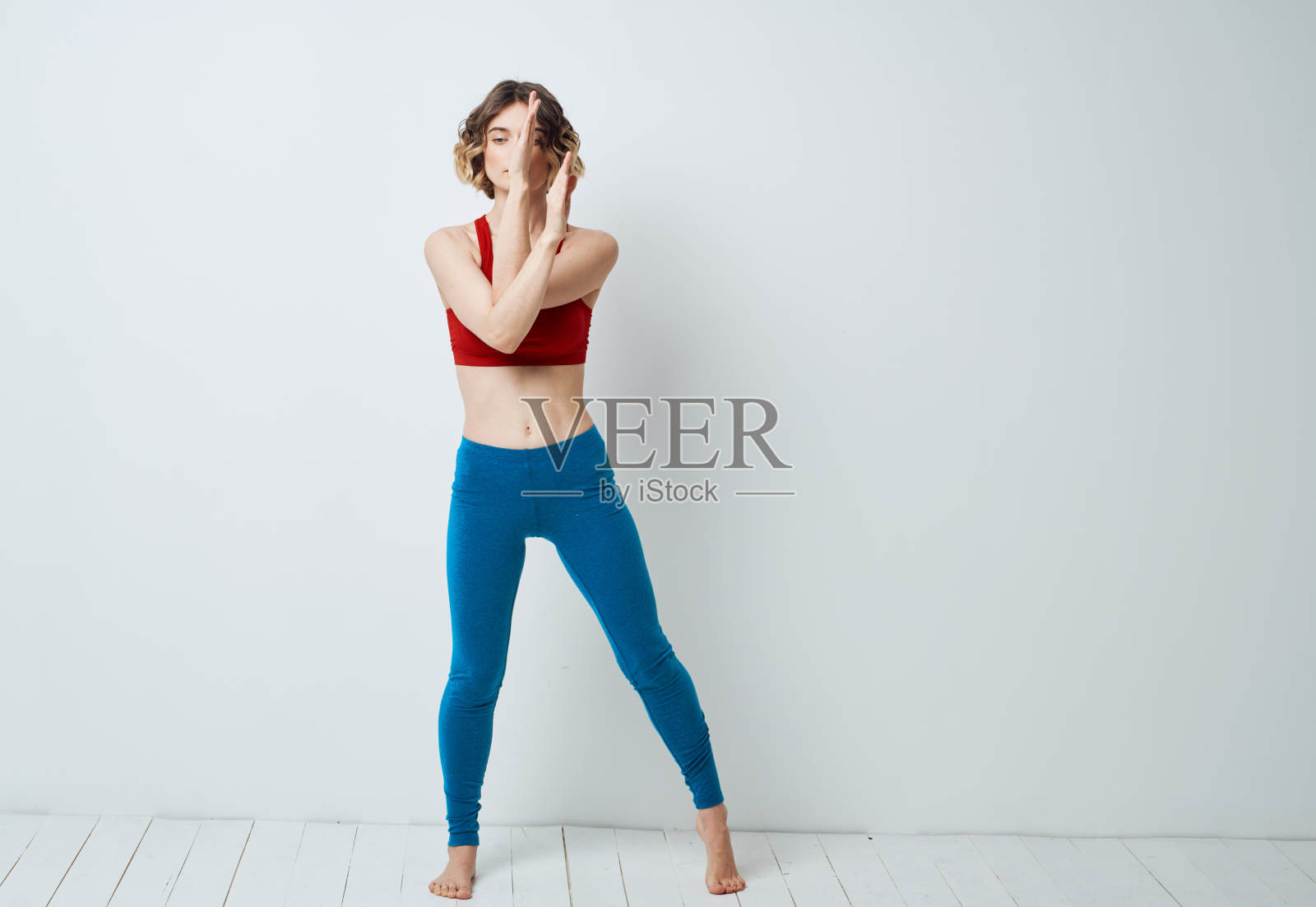 一个穿着蓝色紧身裤的女人在瑜伽体式的浅色背景下做运动照片摄影图片
