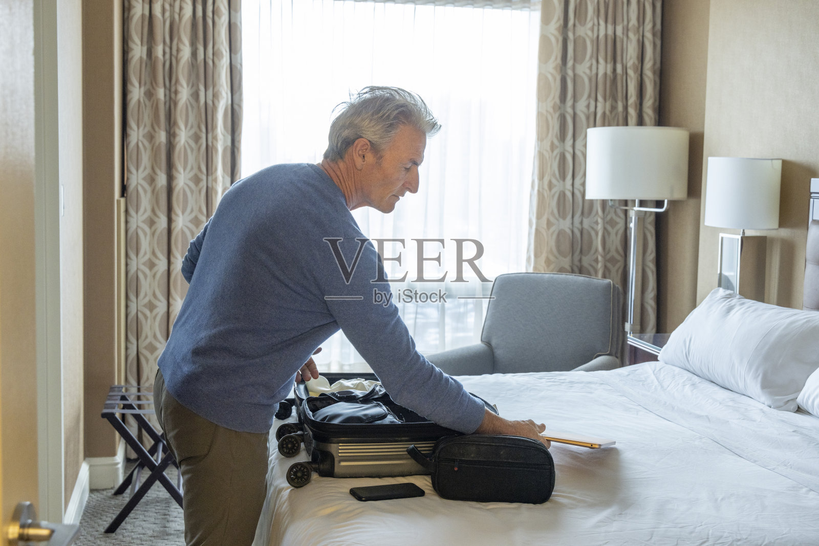 成熟的男人打开床上的行李箱照片摄影图片