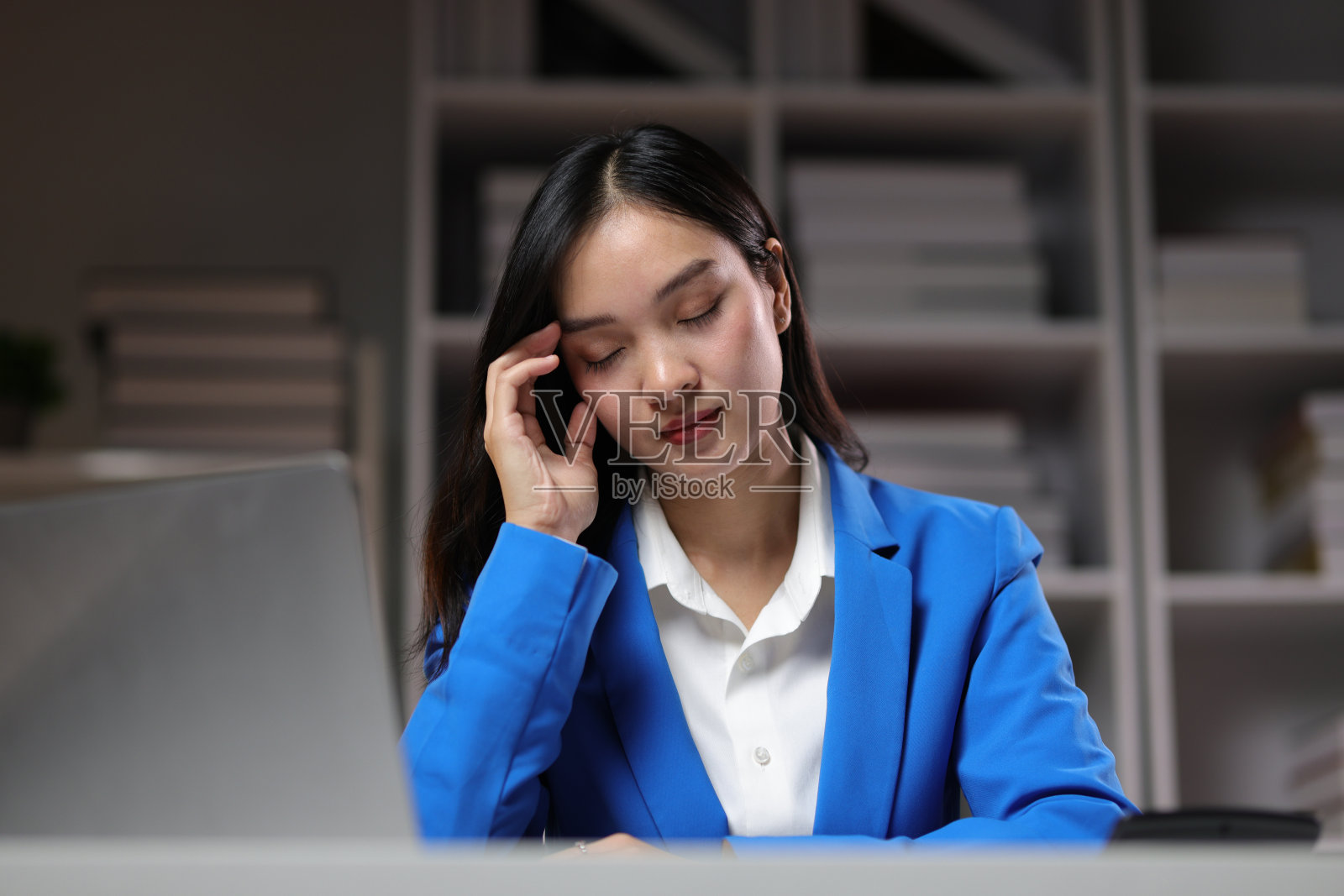 压力和疲劳的亚洲年轻女商人晚上在办公室加班时感到头痛。照片摄影图片