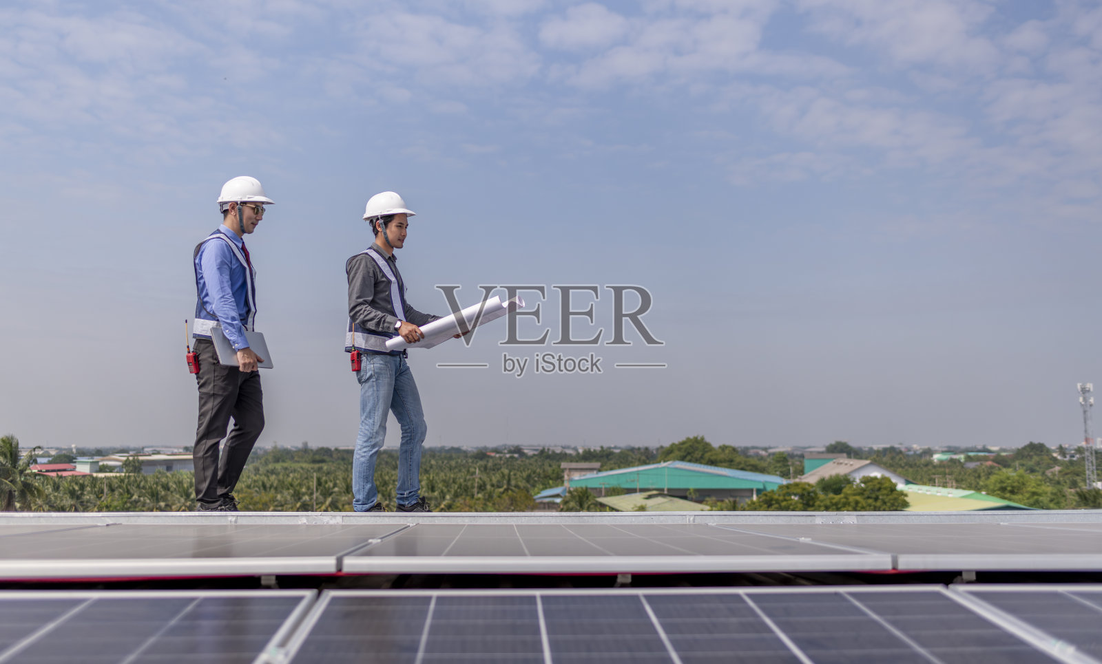 工程师走在屋顶上，拿着设备箱和无线电通讯检查太阳能电池板，太阳能电池是智能电网生态能源阳光替代发电厂的概念。照片摄影图片