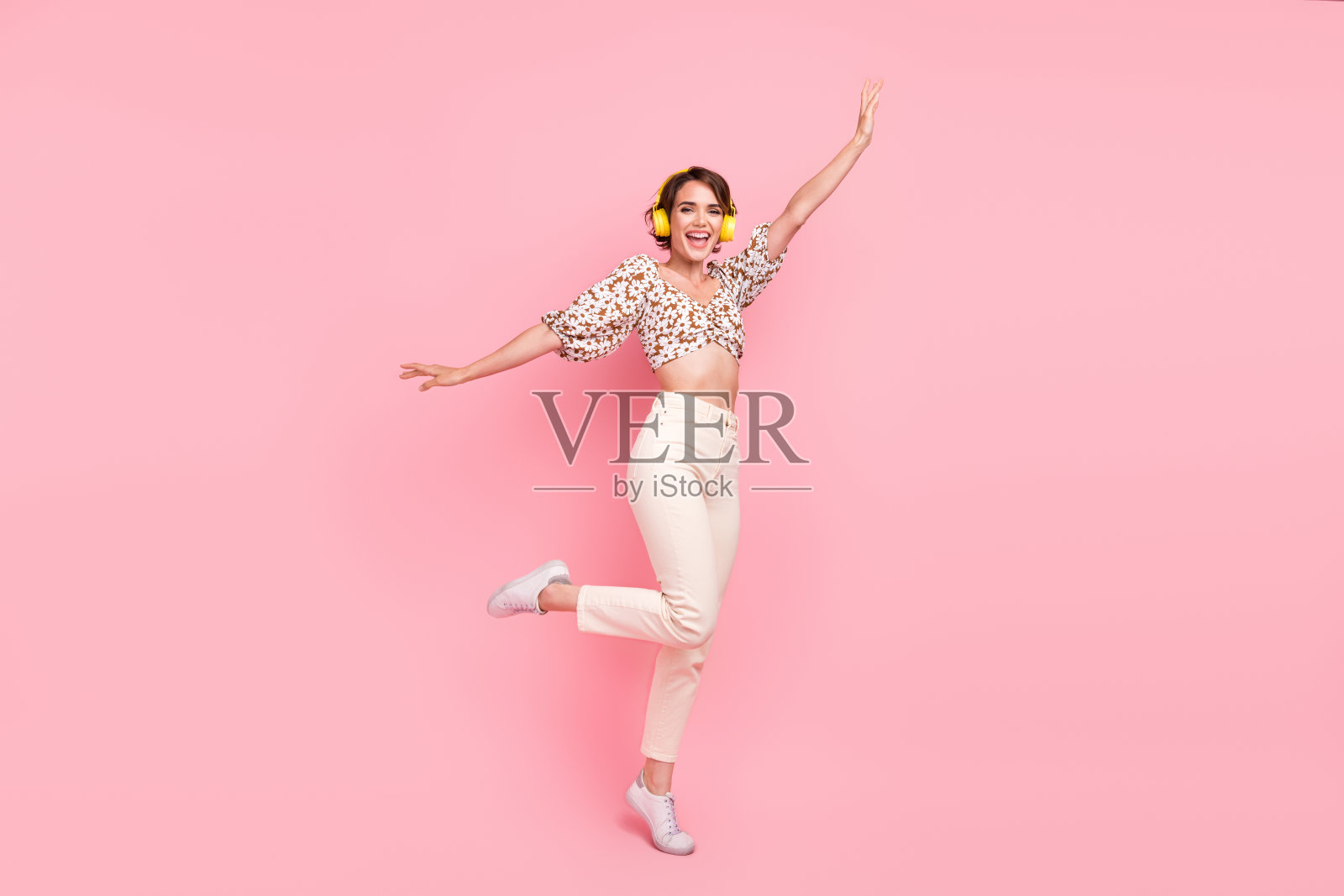 心情好可爱的女孩穿着时髦的衬衫，戴着耳机，手掌像翅膀一样孤立在粉红色的背景照片摄影图片