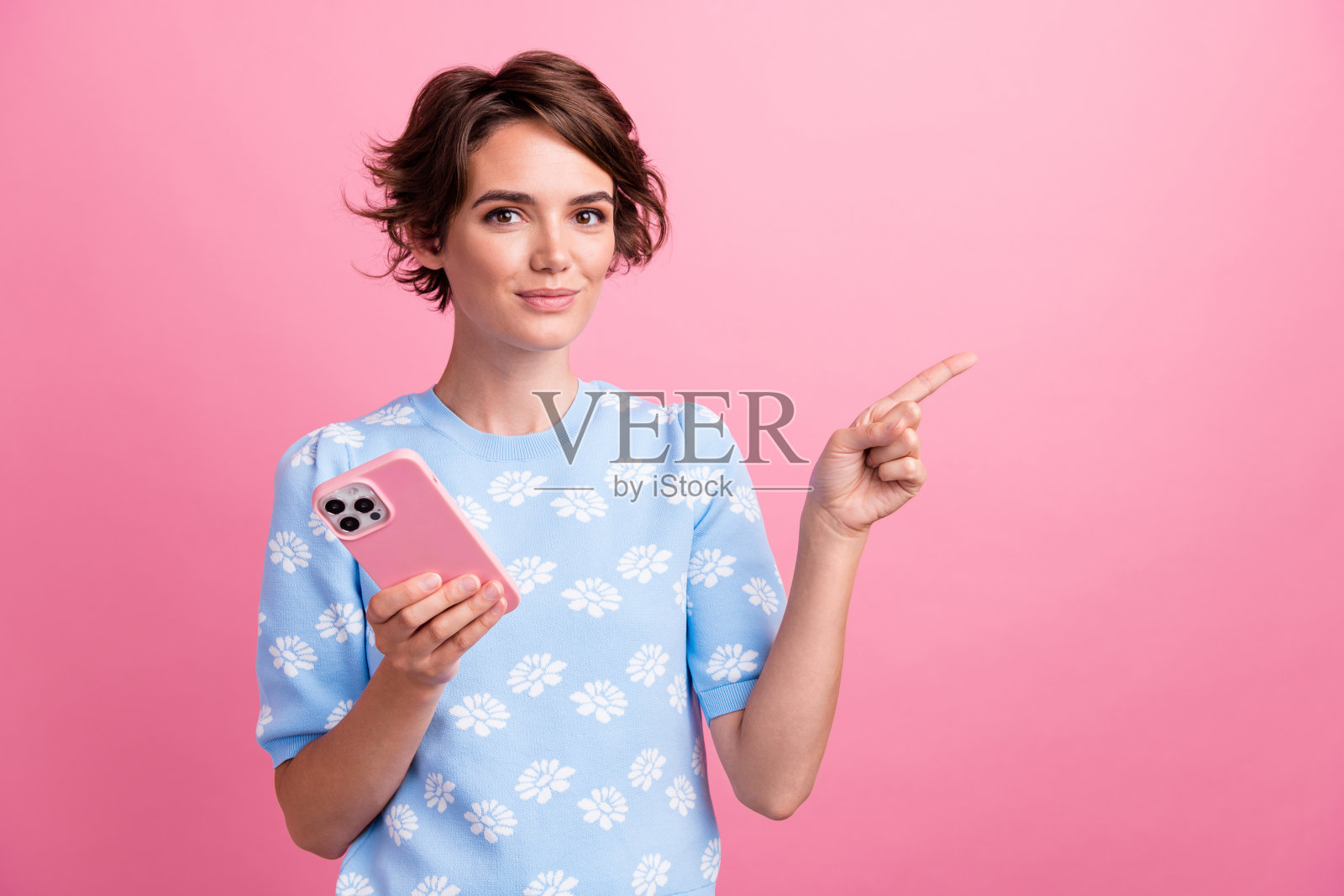 华丽的人的肖像持有智能手机直接手指空白的空间，并隔离在粉红色的背景照片摄影图片