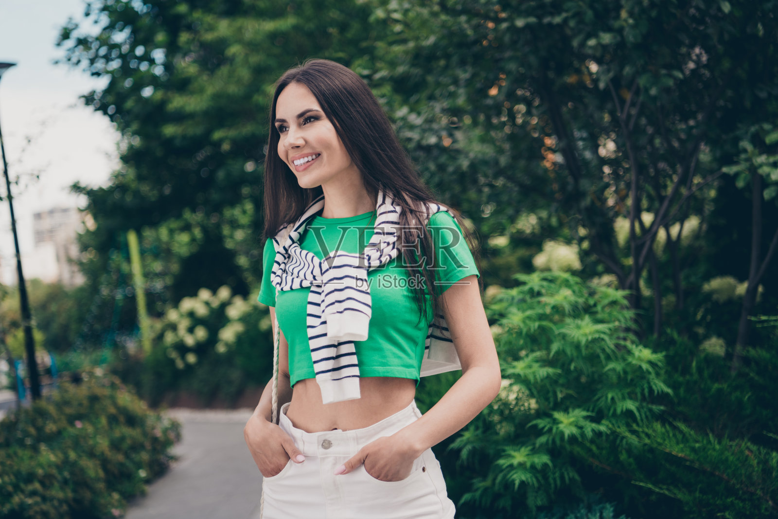 侧视图肖像迷人的完美梦幻的黑发女士把手放在裤子口袋里看着盛开的花园照片摄影图片