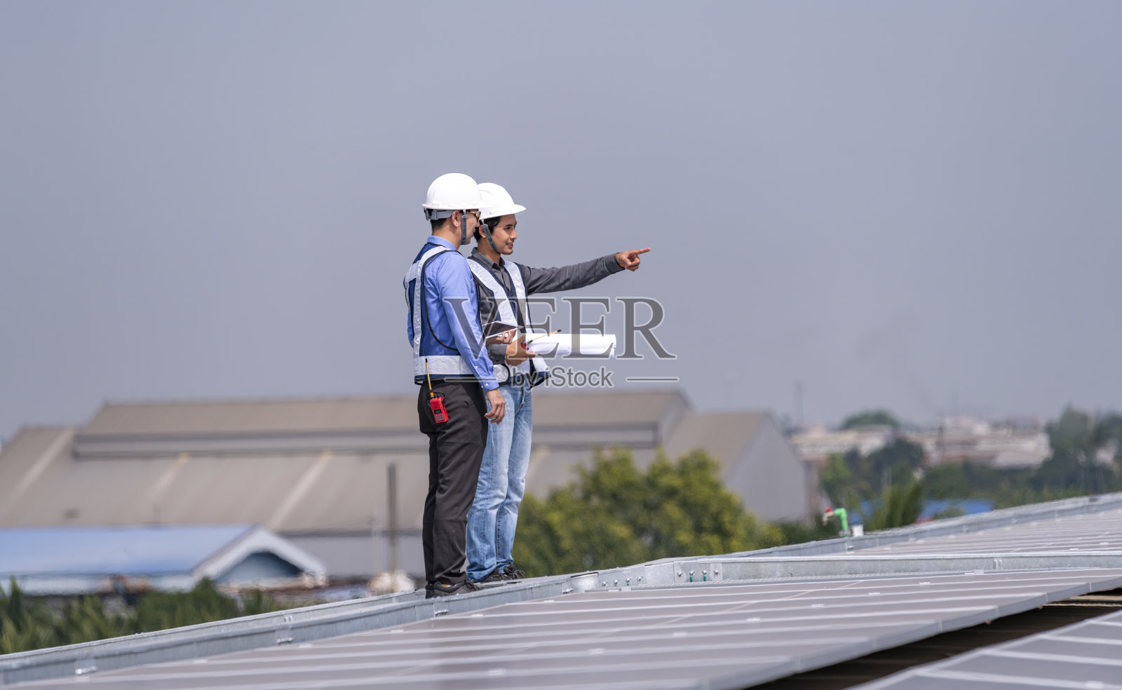 工程师走在屋顶上，拿着设备箱和无线电通讯检查太阳能电池板，太阳能电池是智能电网生态能源阳光替代发电厂的概念。照片摄影图片
