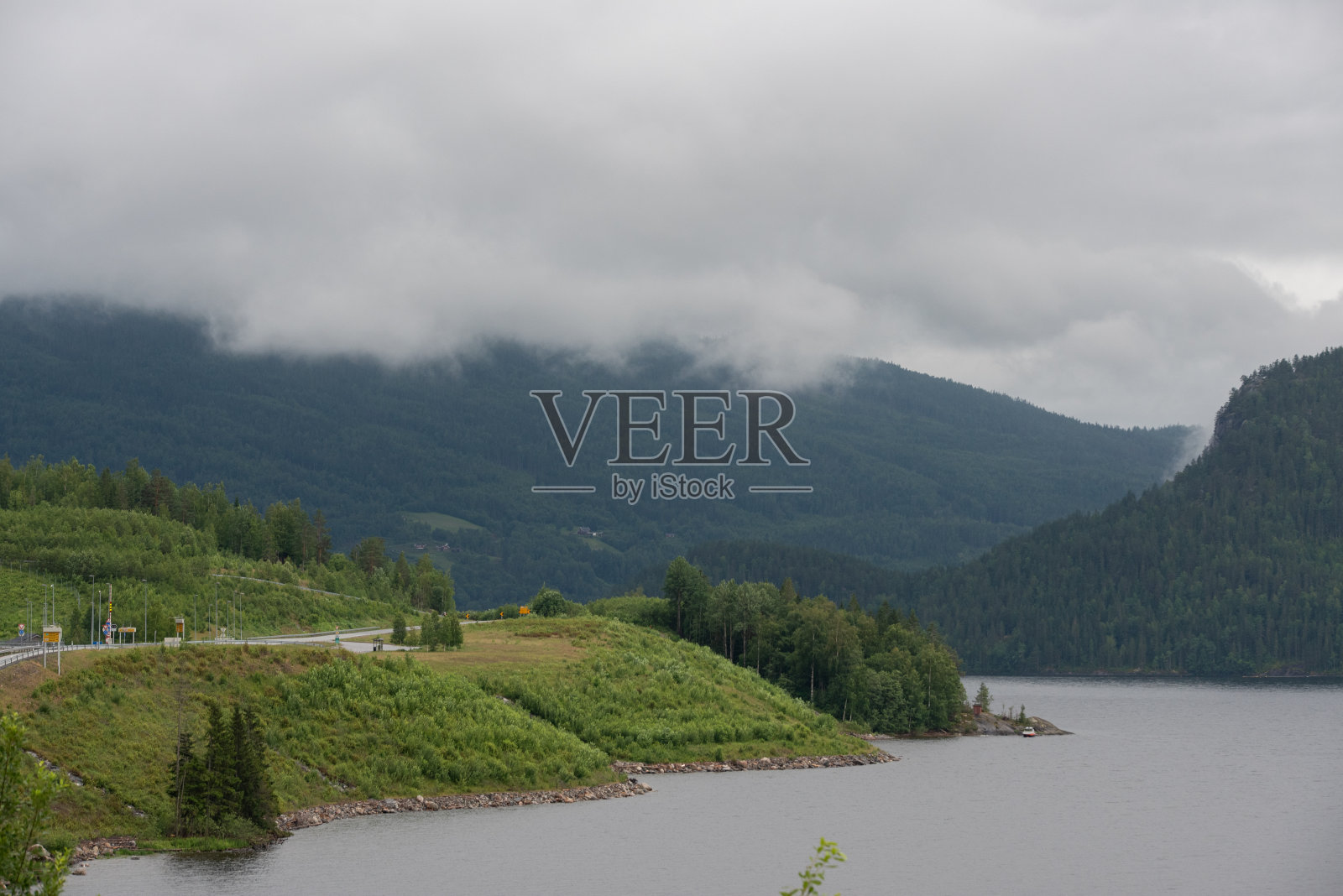 挪威的一条河流，在雾天沿着绿树成荫的山脉和高速公路流动。照片摄影图片