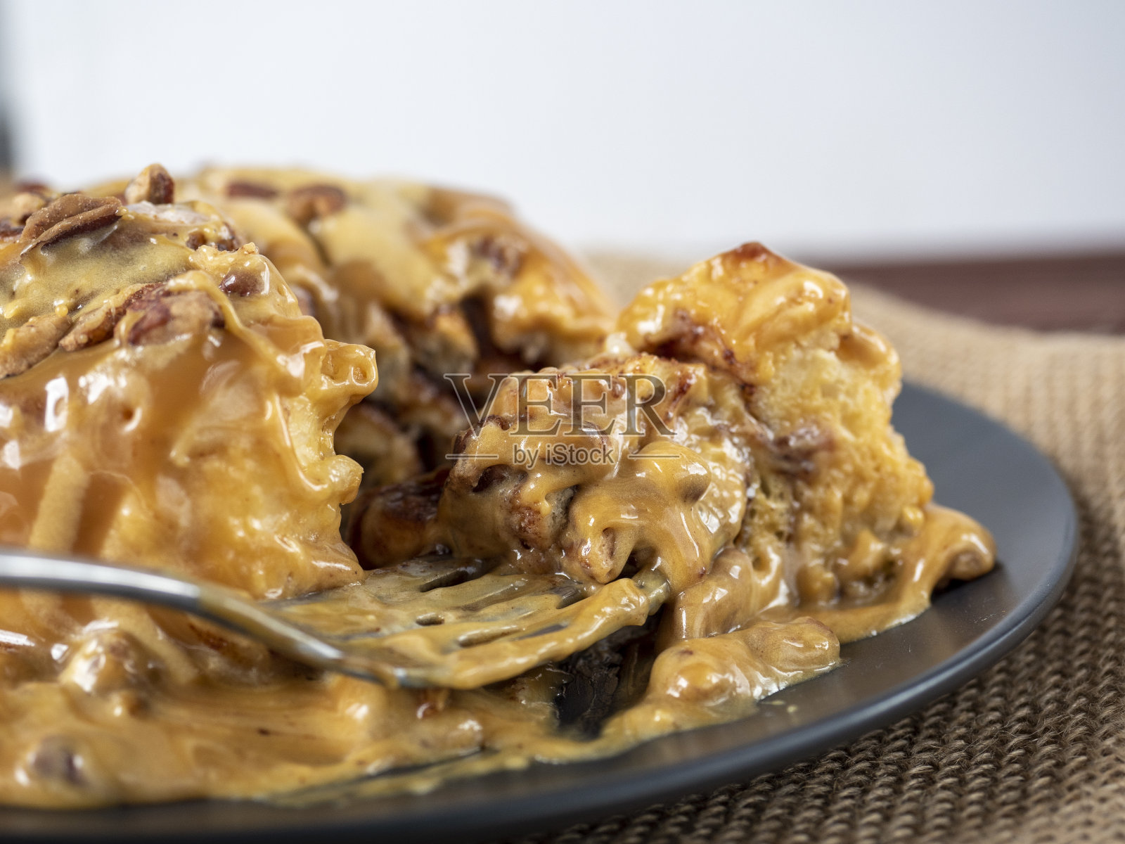 一只黑色盘子和一张亚麻餐巾上放着一个肉桂面包的特写，上面撒着焦糖，装饰着坚果。侧视图，一块甜点是用叉子取下的。有选择性的重点照片摄影图片