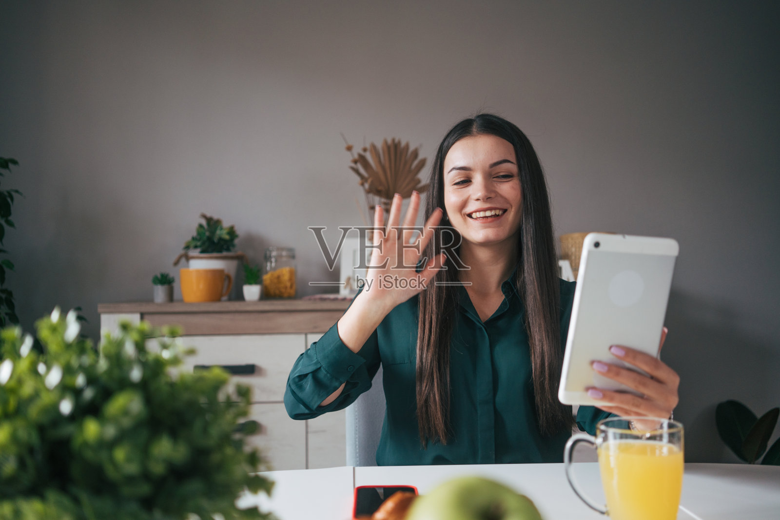 一个年轻的女人正坐在客厅的桌子旁，使用着一台数码平板电脑。照片摄影图片
