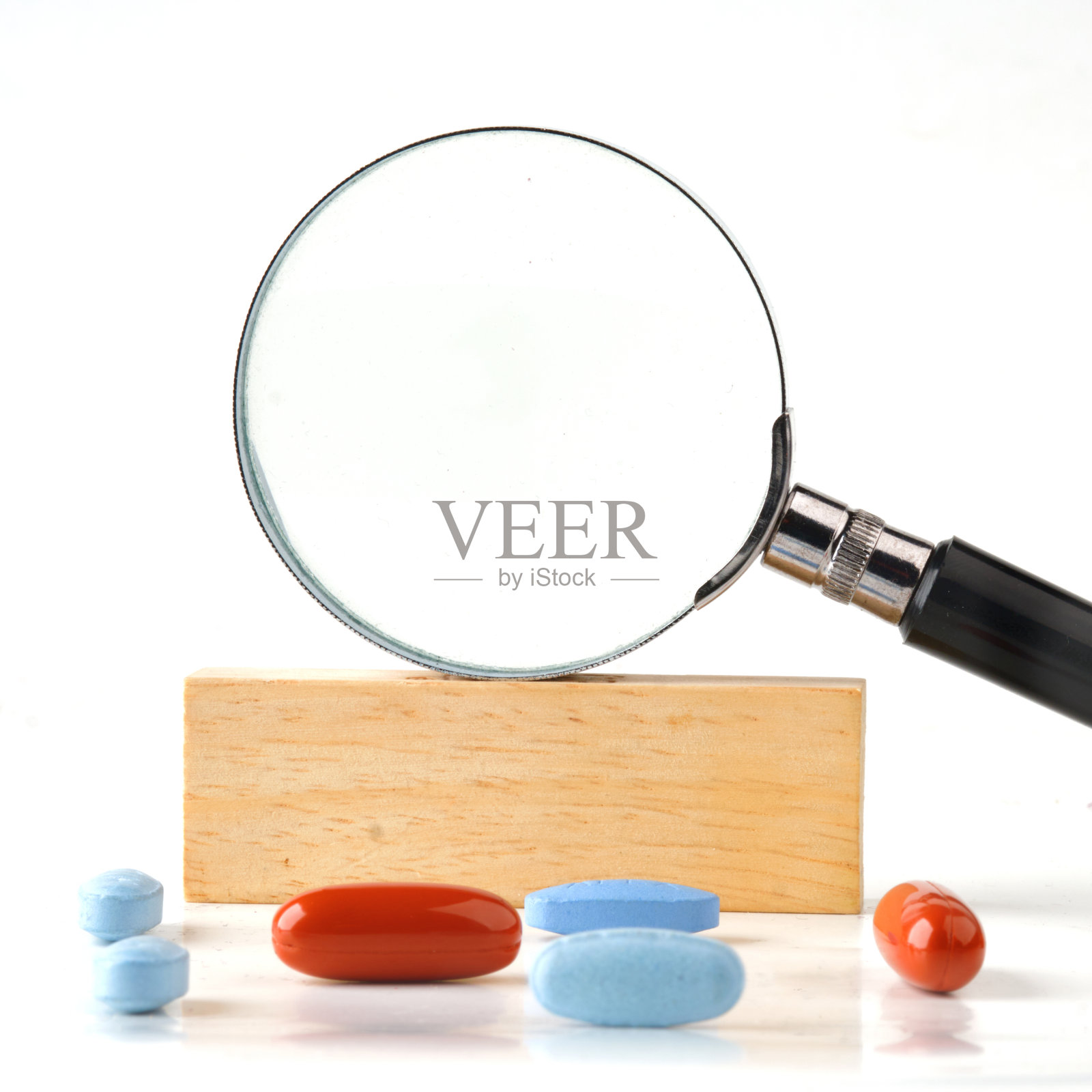 放大镜放在木条上的特写镜头，前景是药丸。一个地方去c照片摄影图片