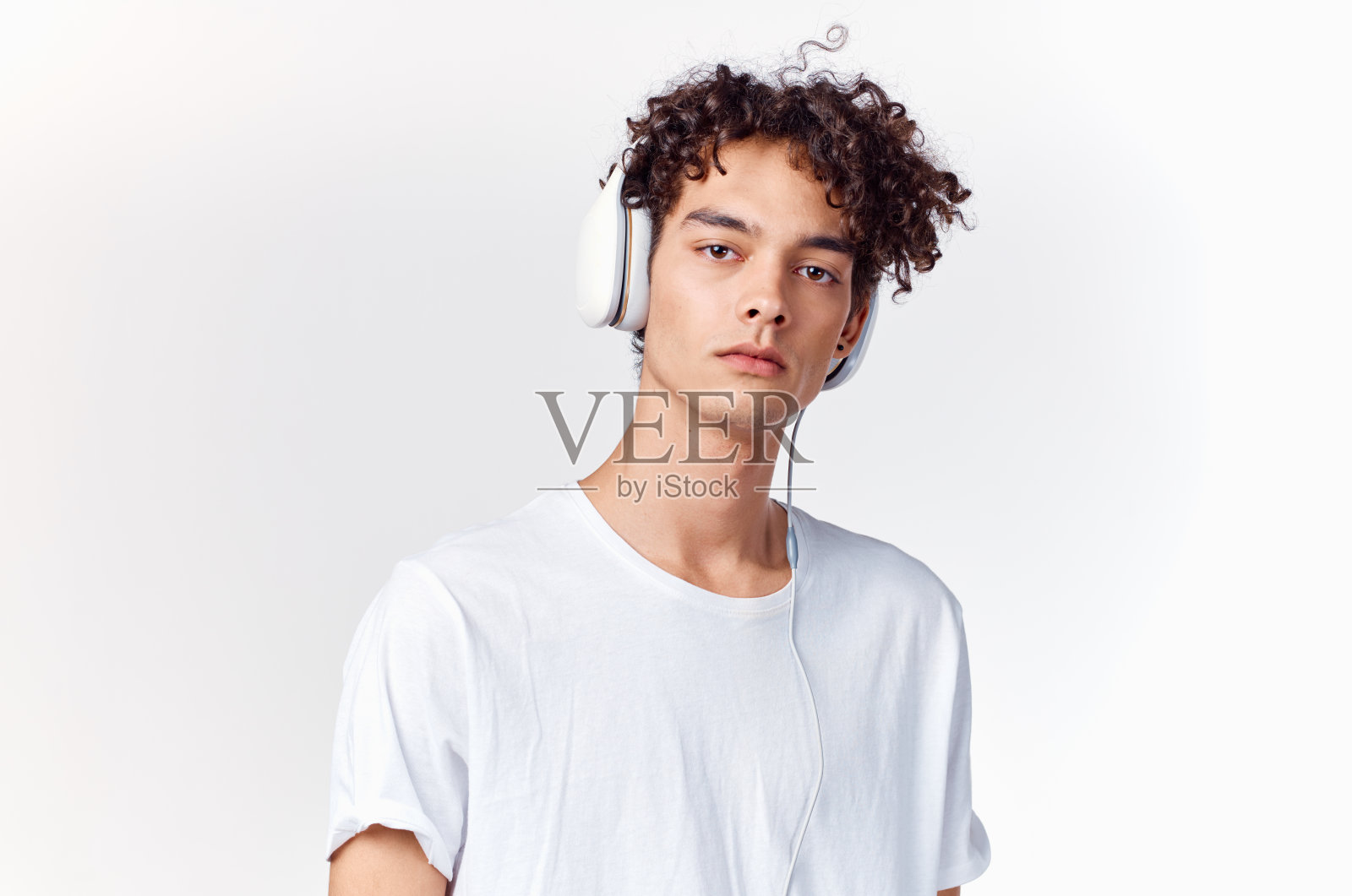 戴着耳机的快乐卷毛男孩在浅色背景的裁剪视图上听音乐照片摄影图片