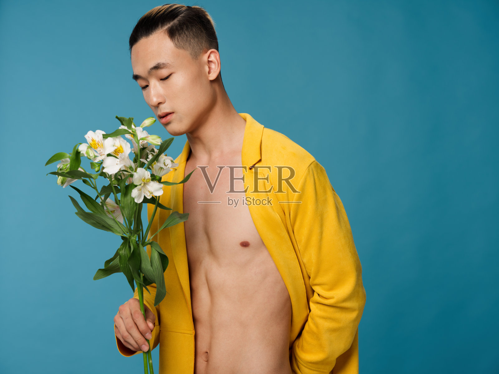 可爱的年轻人穿着黄色的外套和白色的花蓝色的背景节日礼物照片摄影图片