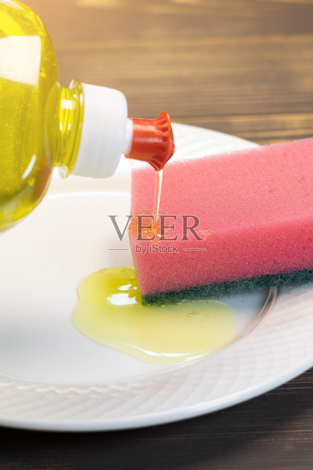 男子正在把黄色的液体洗涤凝胶倒入海绵中，用来清洗白色盘子上的盘子。厨房清洁用品。照片摄影图片