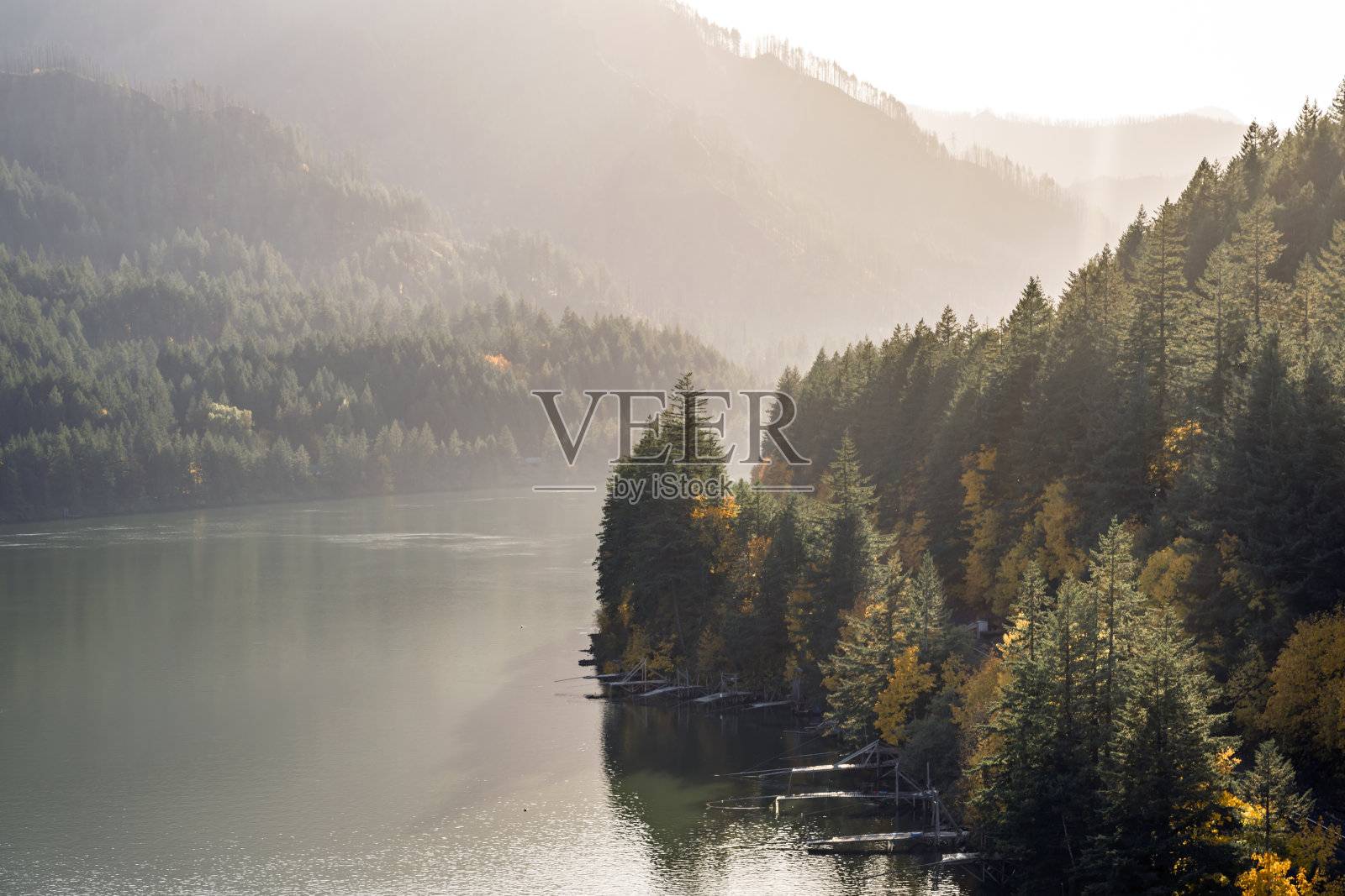 山坡上秋天的绿色和黄色森林的神秘景观在哥伦比亚河平静的水面上反射，还有许多钓鲑鱼的码头照片摄影图片